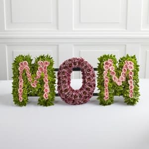 Floral arrangement spelling MOM with pink flowers and green foliage