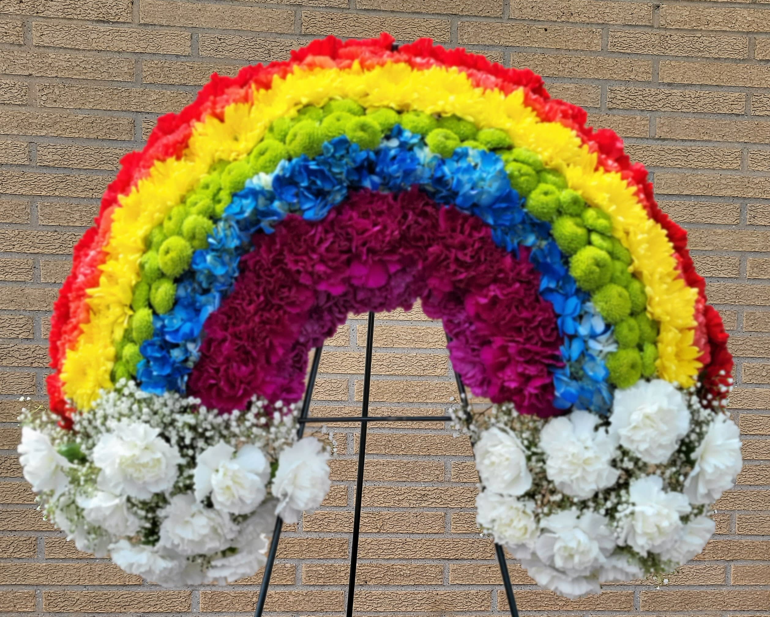 Rainbow floral standing spray on an easel with white flowers at the base