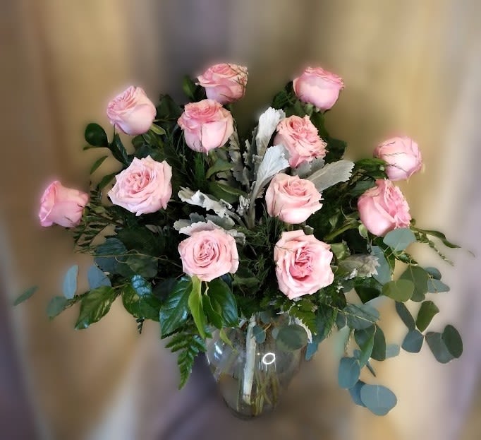 Pink roses arranged in a clear glass vase with mixed greenery.