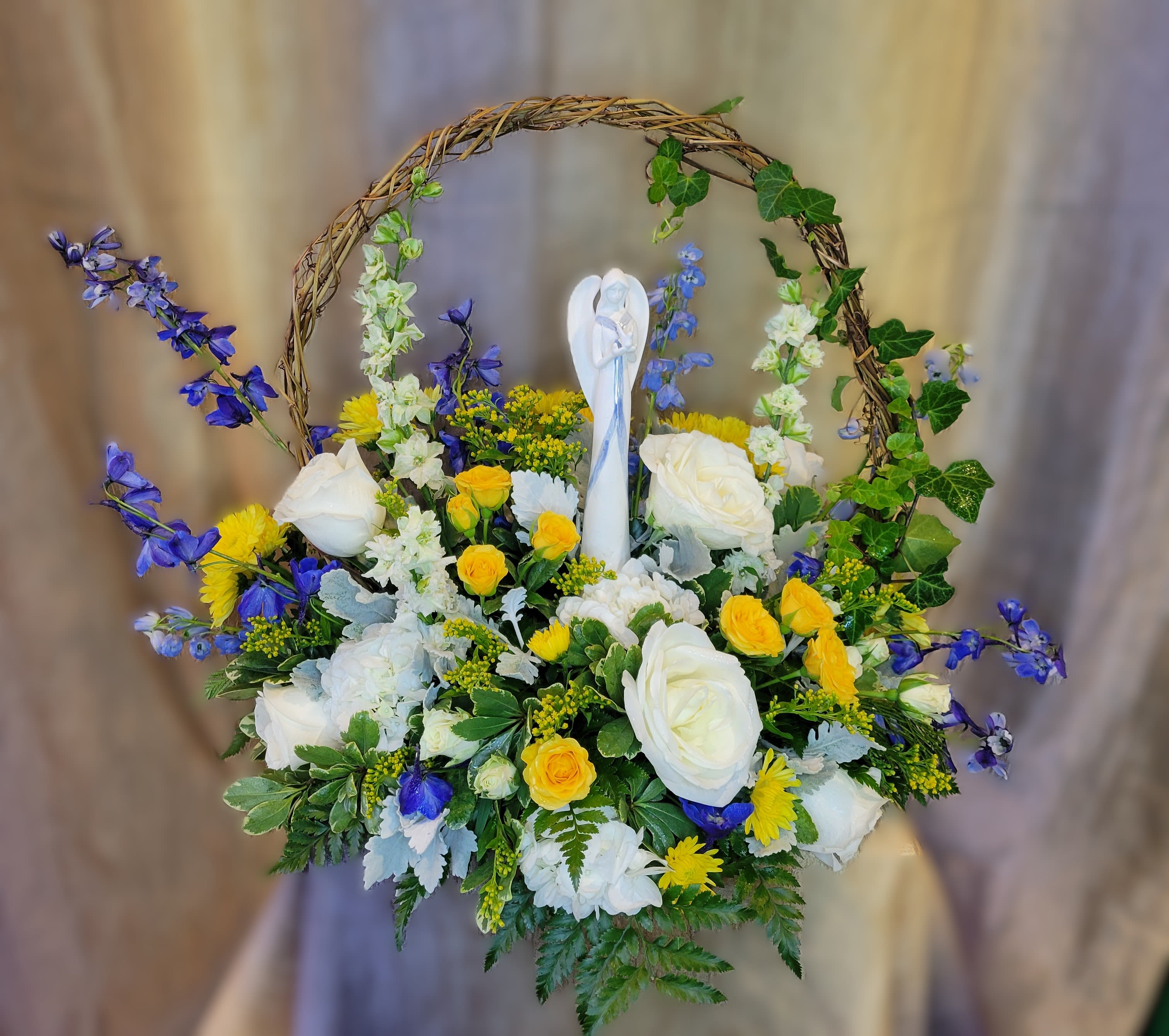 Basket of white and yellow flowers with blue accents and a small angel figurine