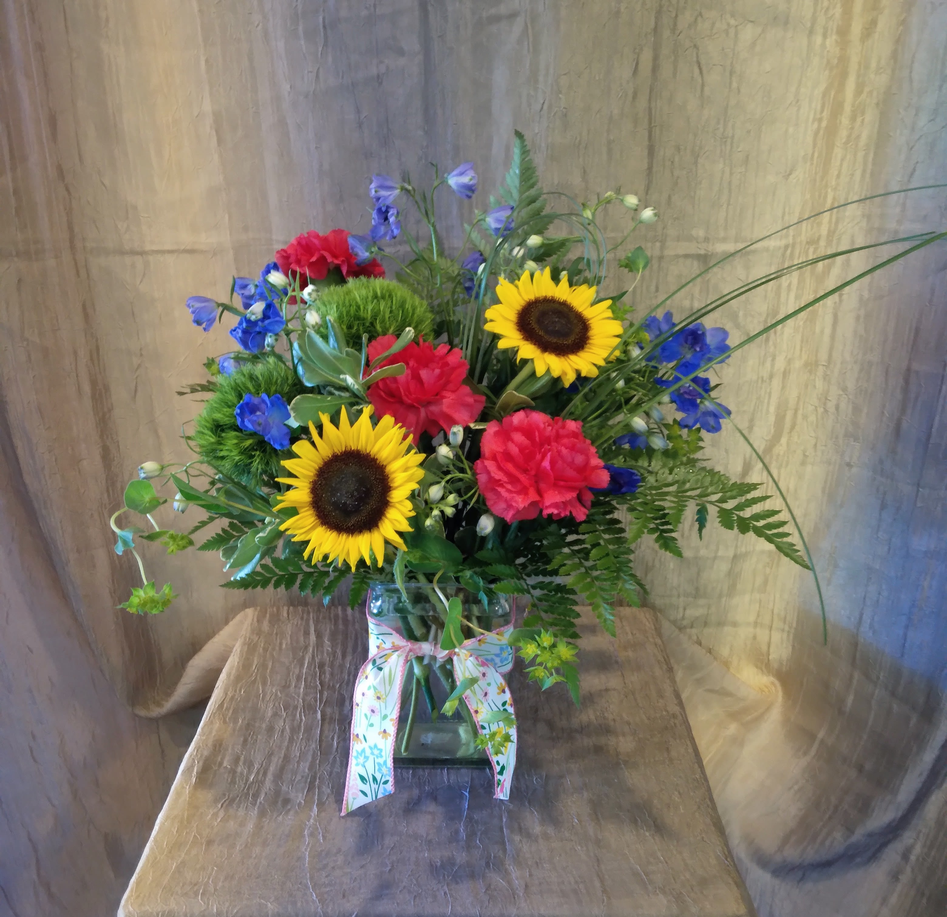 Our Sunlit Garden ~ Flower A Day - This bouquet brings the bright colors of the garden to your table! Featuring sunflowers and brightly colored carnations, this design is sure to deliver the sunshine to your recipient.