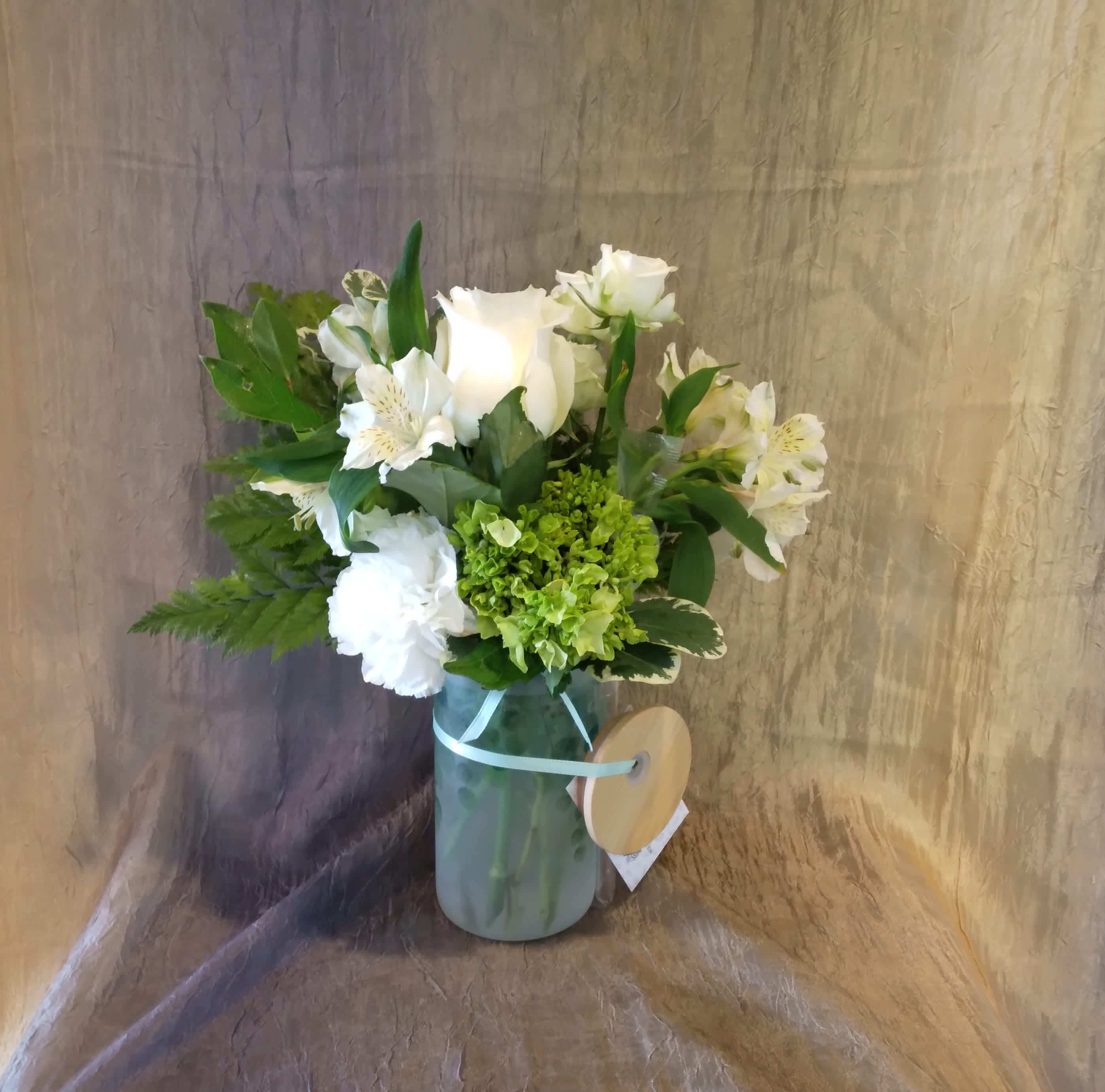 White roses and alstroemeria in a glass vase with green hydrangea