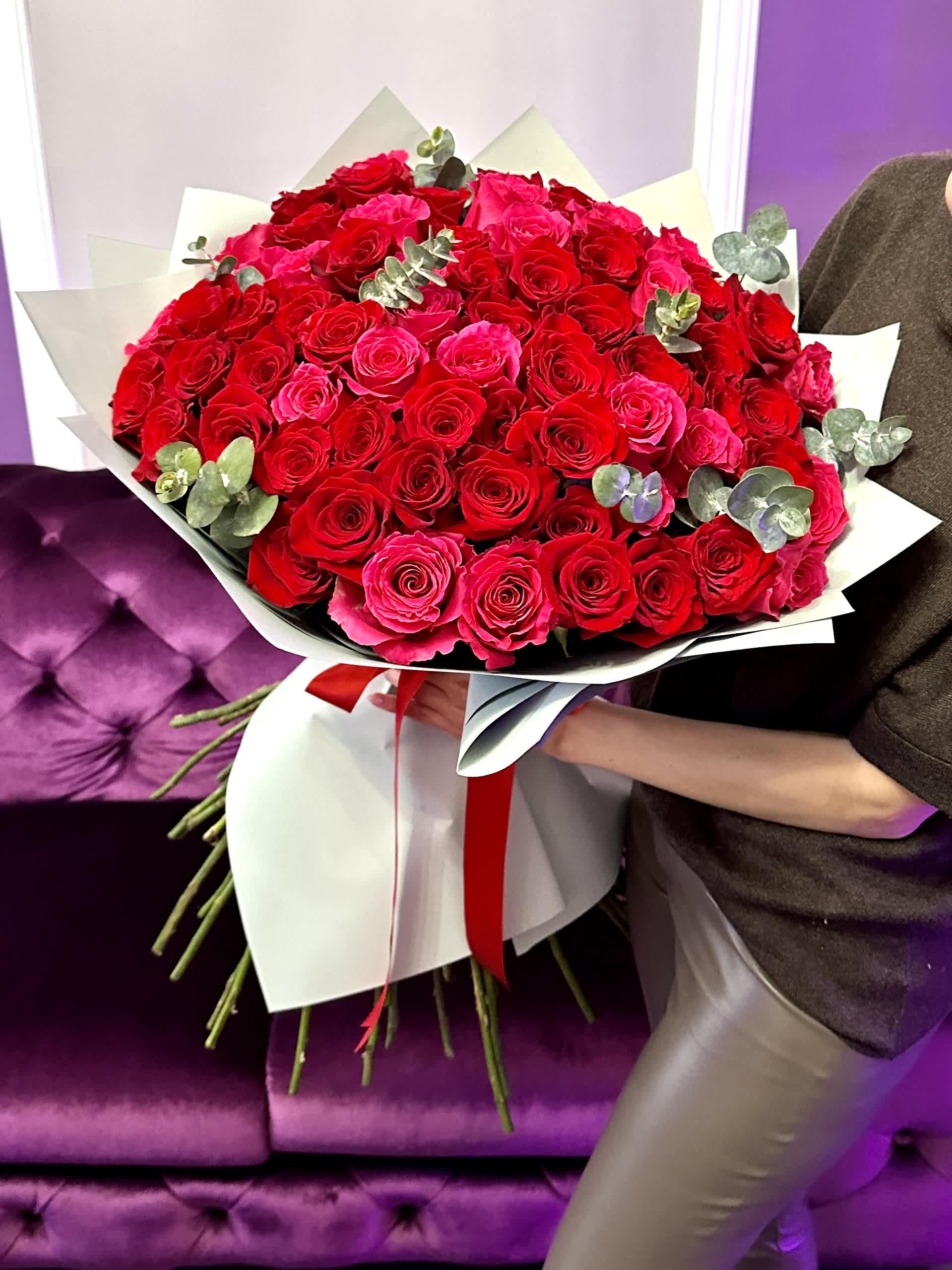 Large hand-tied bouquet of red and hot pink roses wrapped in white paper with a red ribbon.