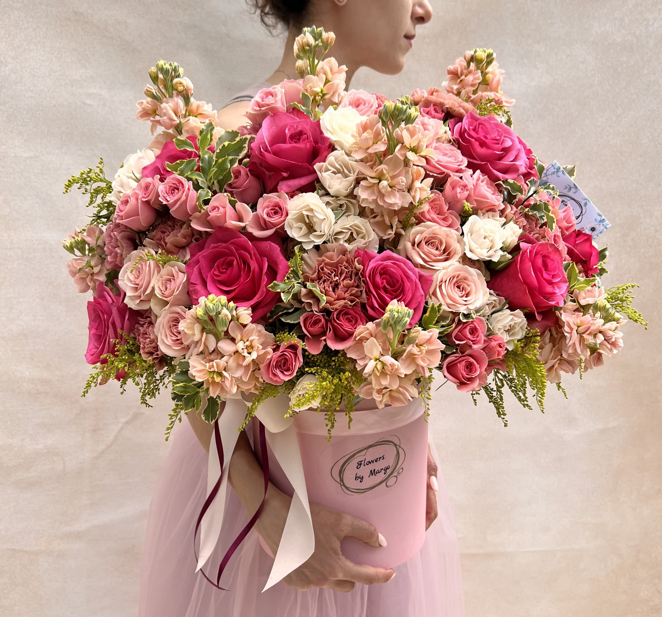 Large pink hatbox arrangement of hot pink and blush roses and mixed flowers held by a woman.