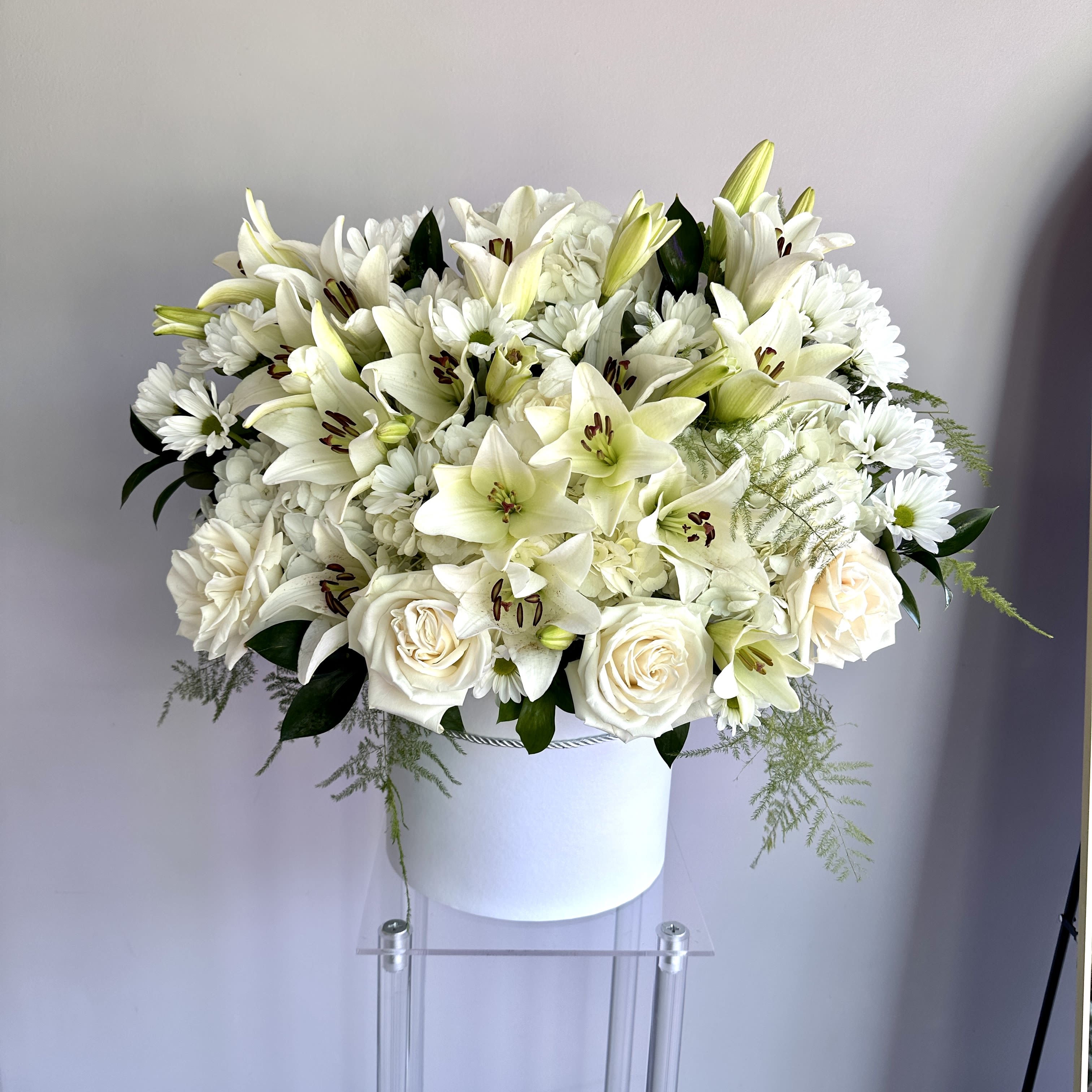 Round arrangement of white lilies, roses, and mums in a white hatbox-style container