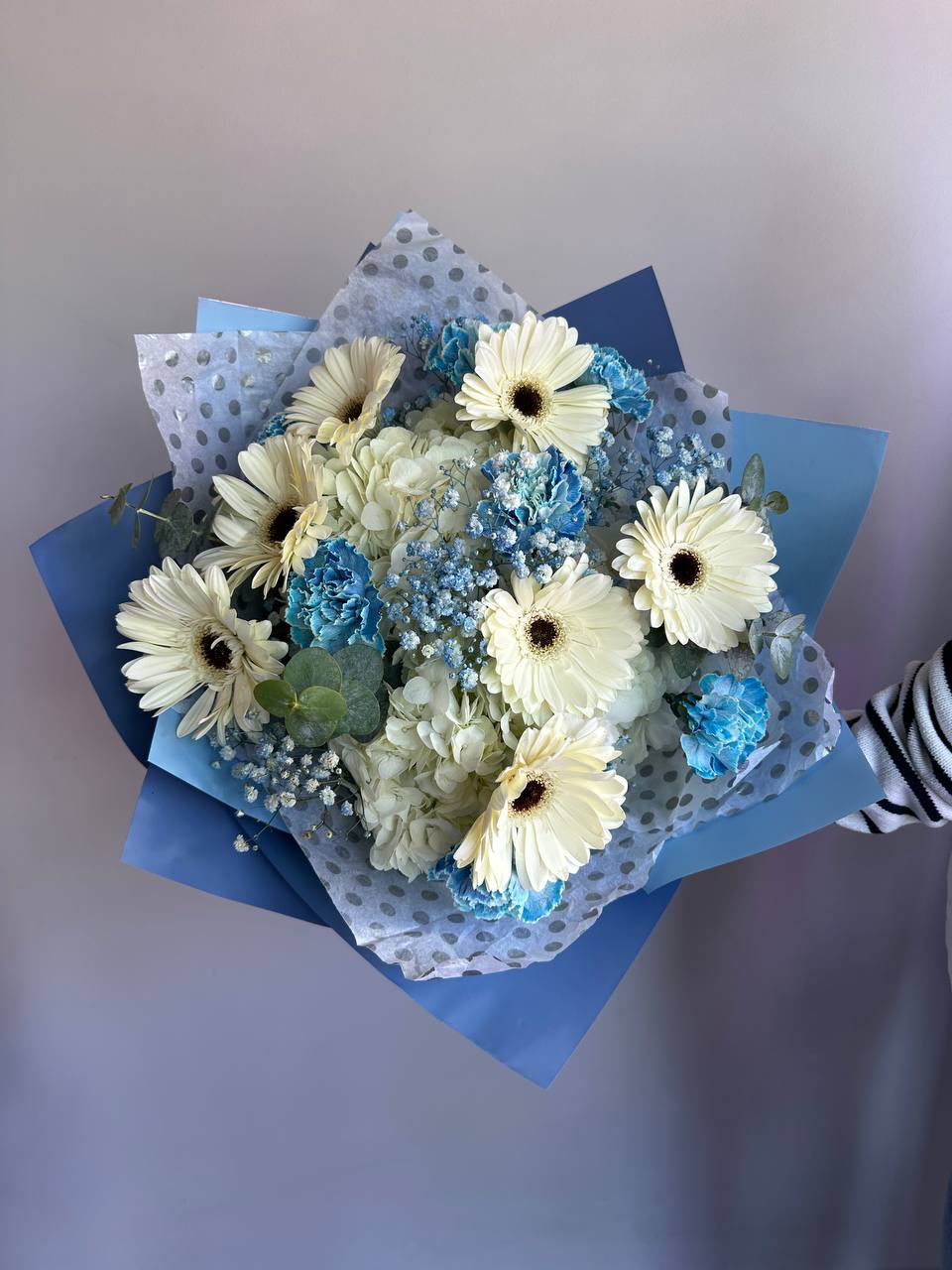 Hand-tied bouquet of white gerbera daisies and blue flowers wrapped in blue and polka dot paper