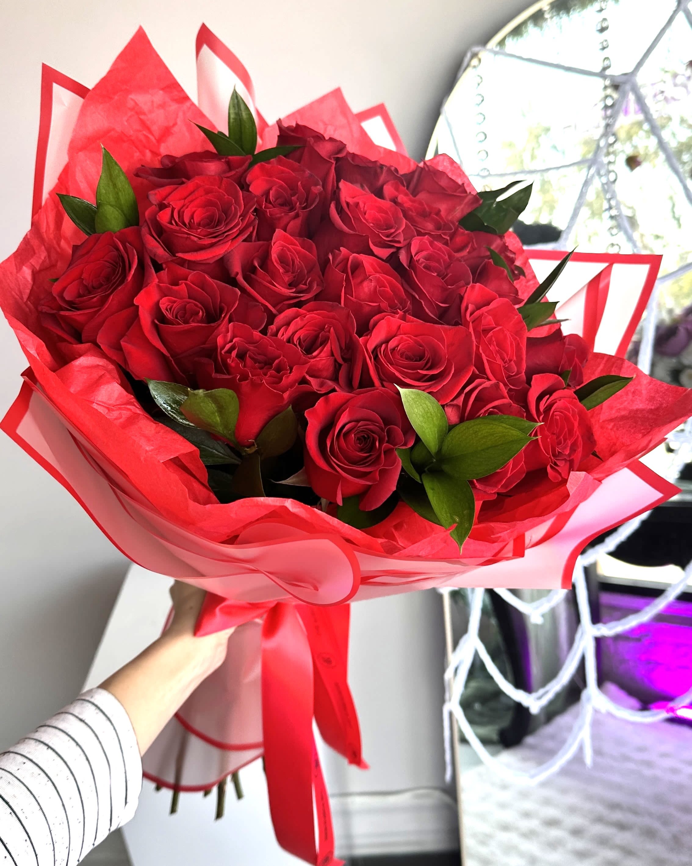 Hand-tied bouquet of red roses wrapped in red paper with a matching ribbon