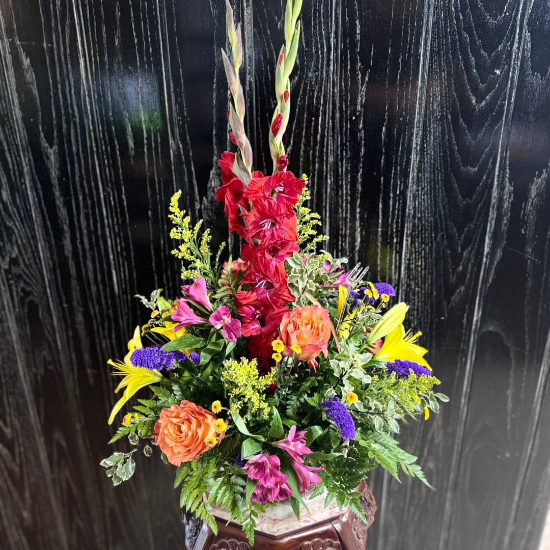 Tall mixed flower arrangement with red gladiolus, orange roses, and yellow lilies in a vase