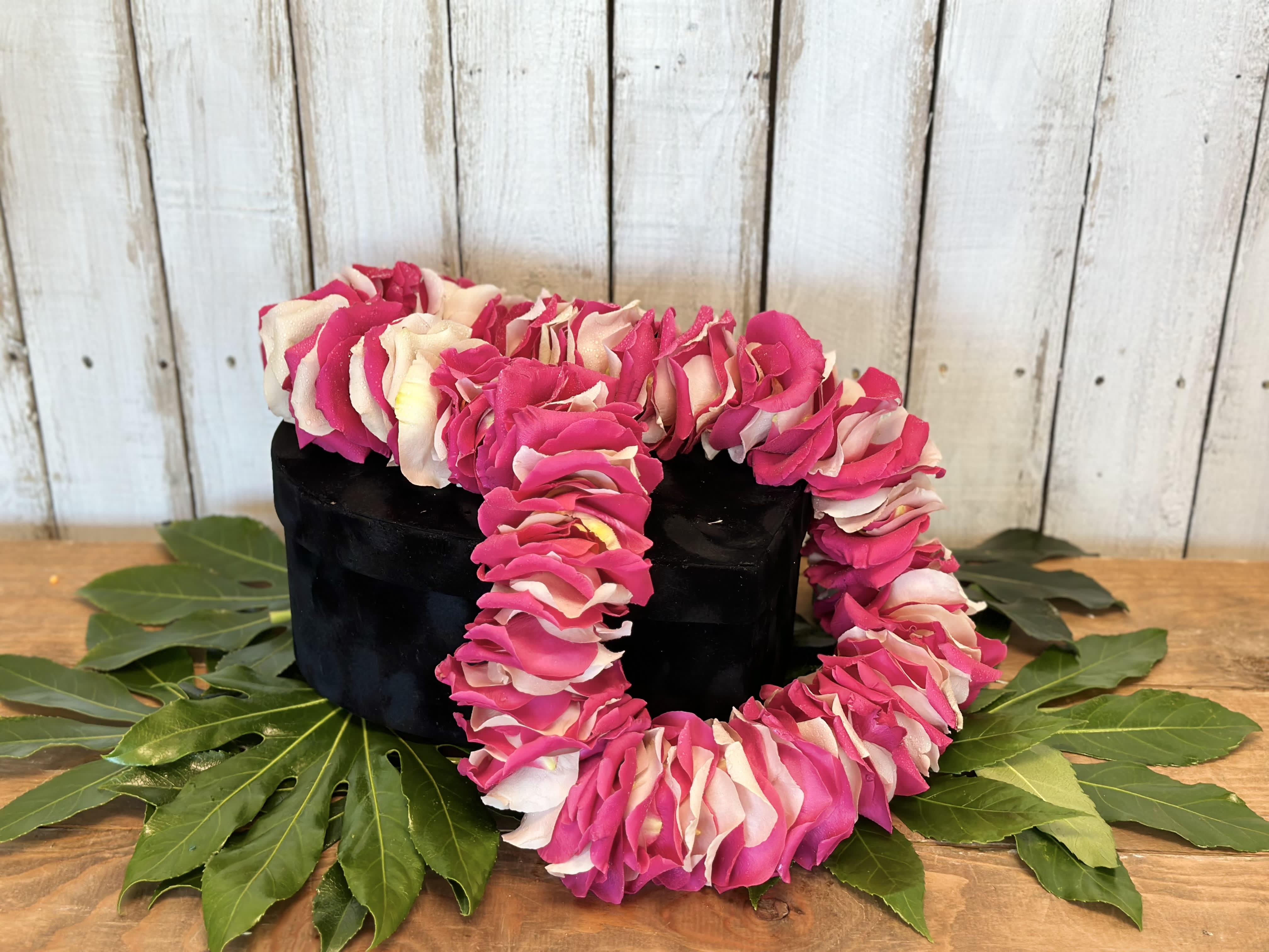 Pink and white flower lei draped over a black box on green leaves