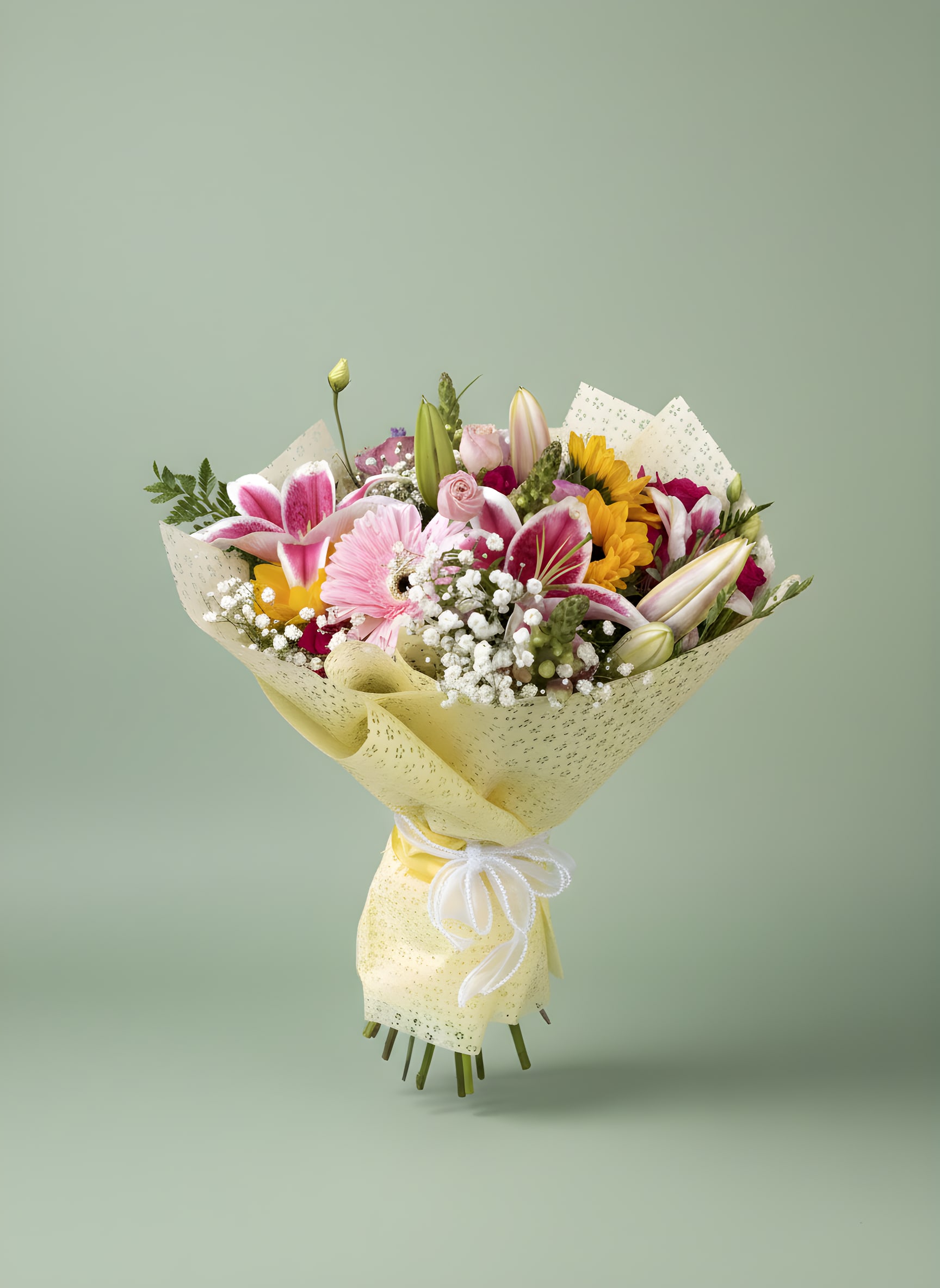 Mixed bouquet of pink, yellow, and white flowers wrapped in pale yellow paper