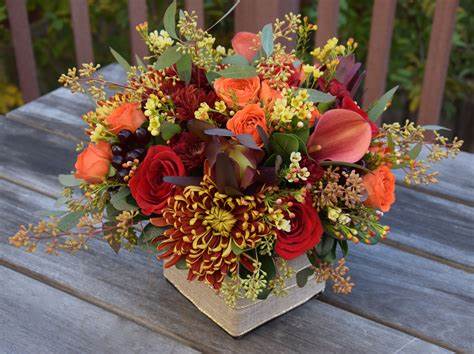 Mixed bouquet of red, orange, and pink flowers in a square vase