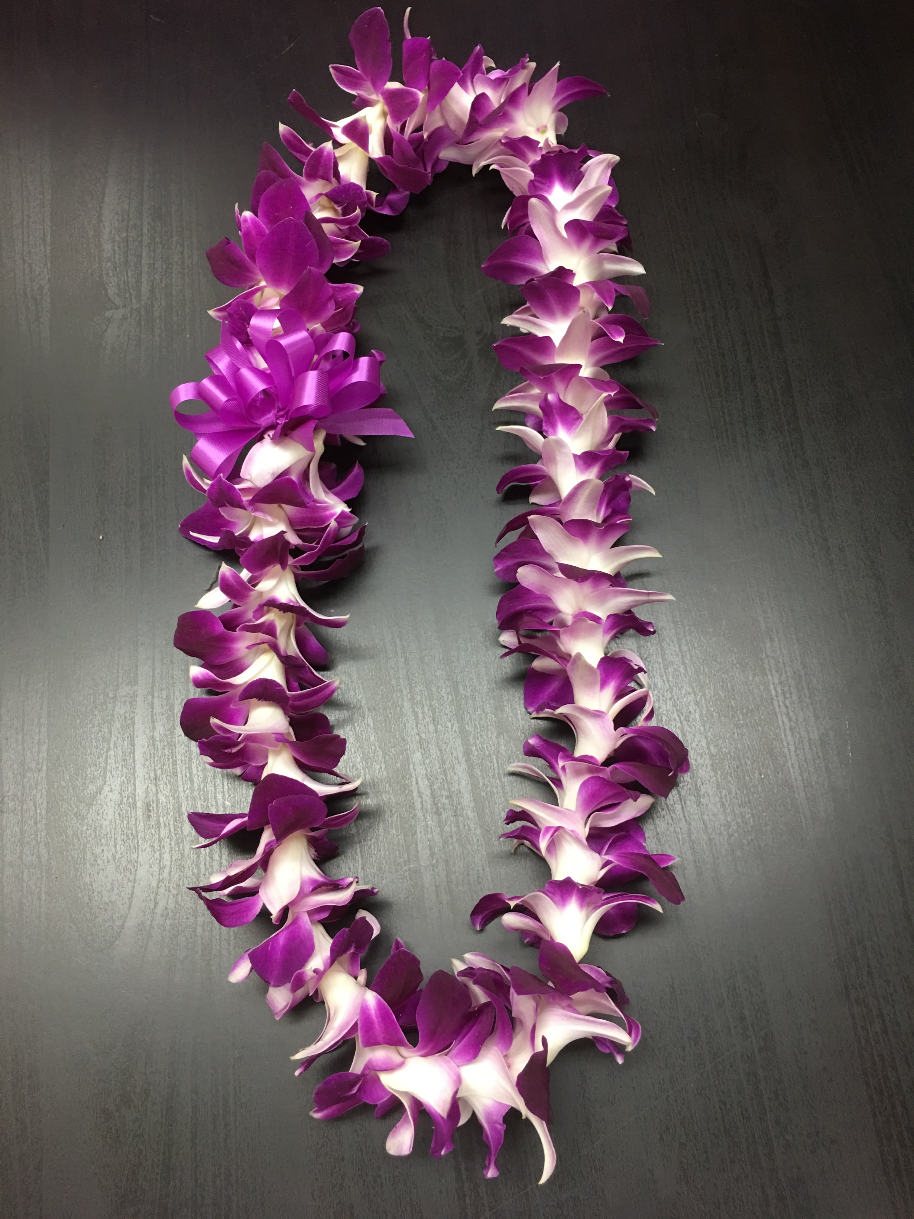 Purple and white orchid lei on a dark surface