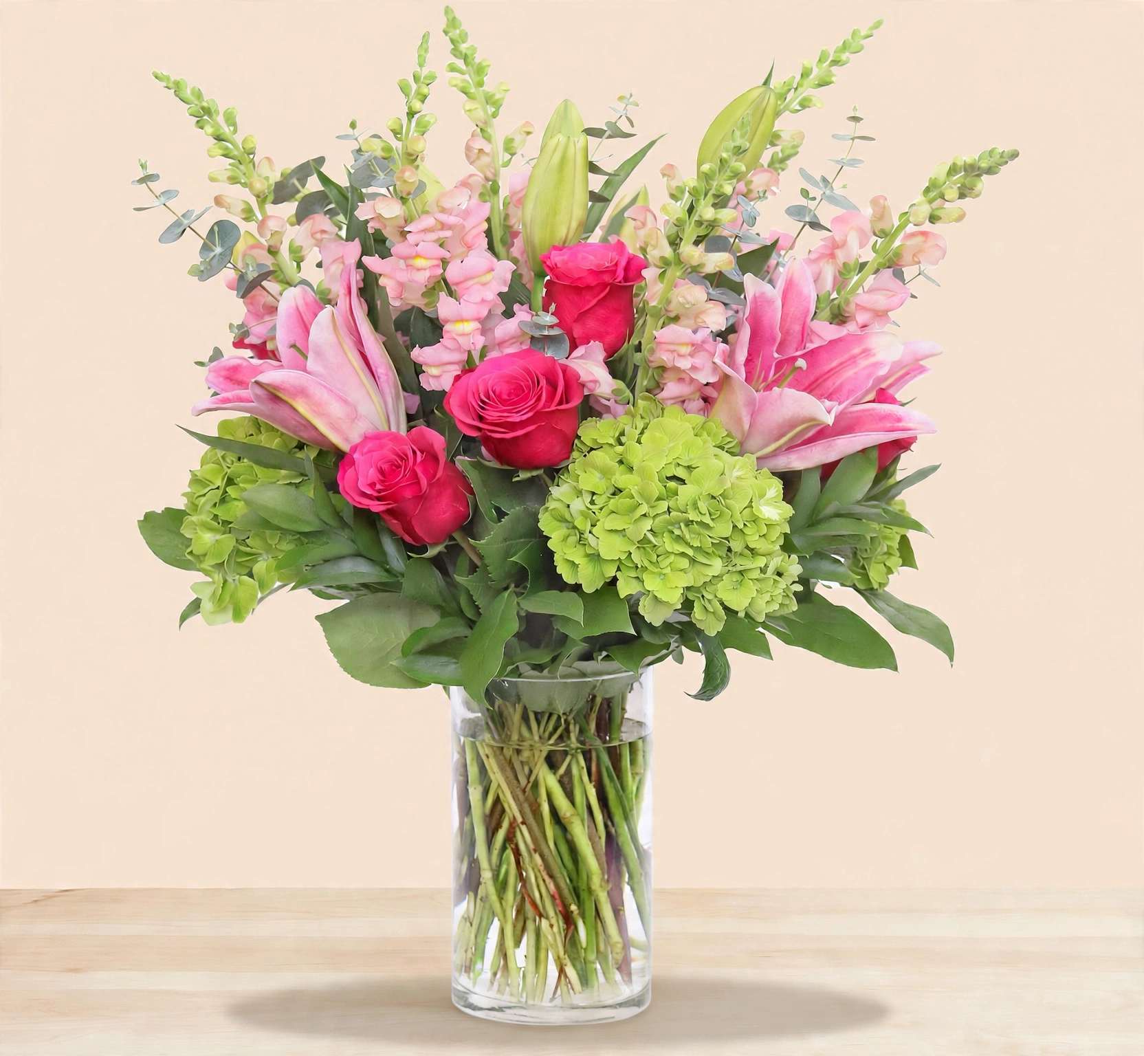 Pink lilies and roses with green hydrangea in a clear glass vase