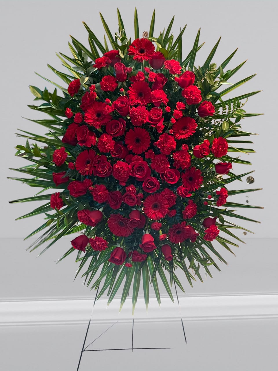 Forever Feelings - Red is the color of love and this standing spray displays it with luxurious style. Red roses and palms come together with other red and greenery to create a beautiful salute.