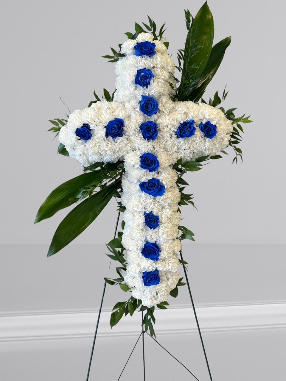 Faith - An all white tribute, this white cross funeral spray is pure and tranquil. Featuring   white  carnations and blue roses, this elegant easel compliments the beauty of life. 