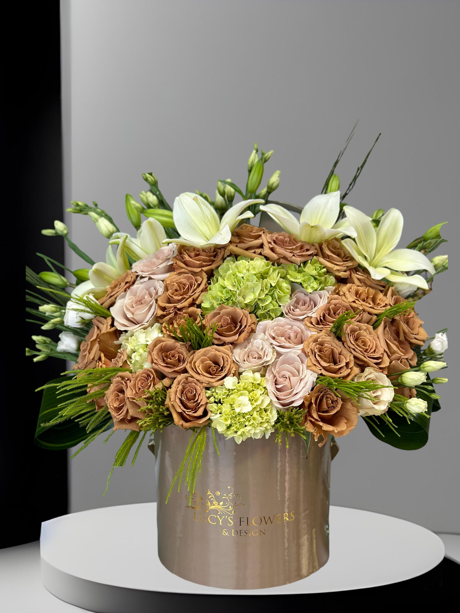 Large bouquet of tan and blush roses with white lilies in a gold box