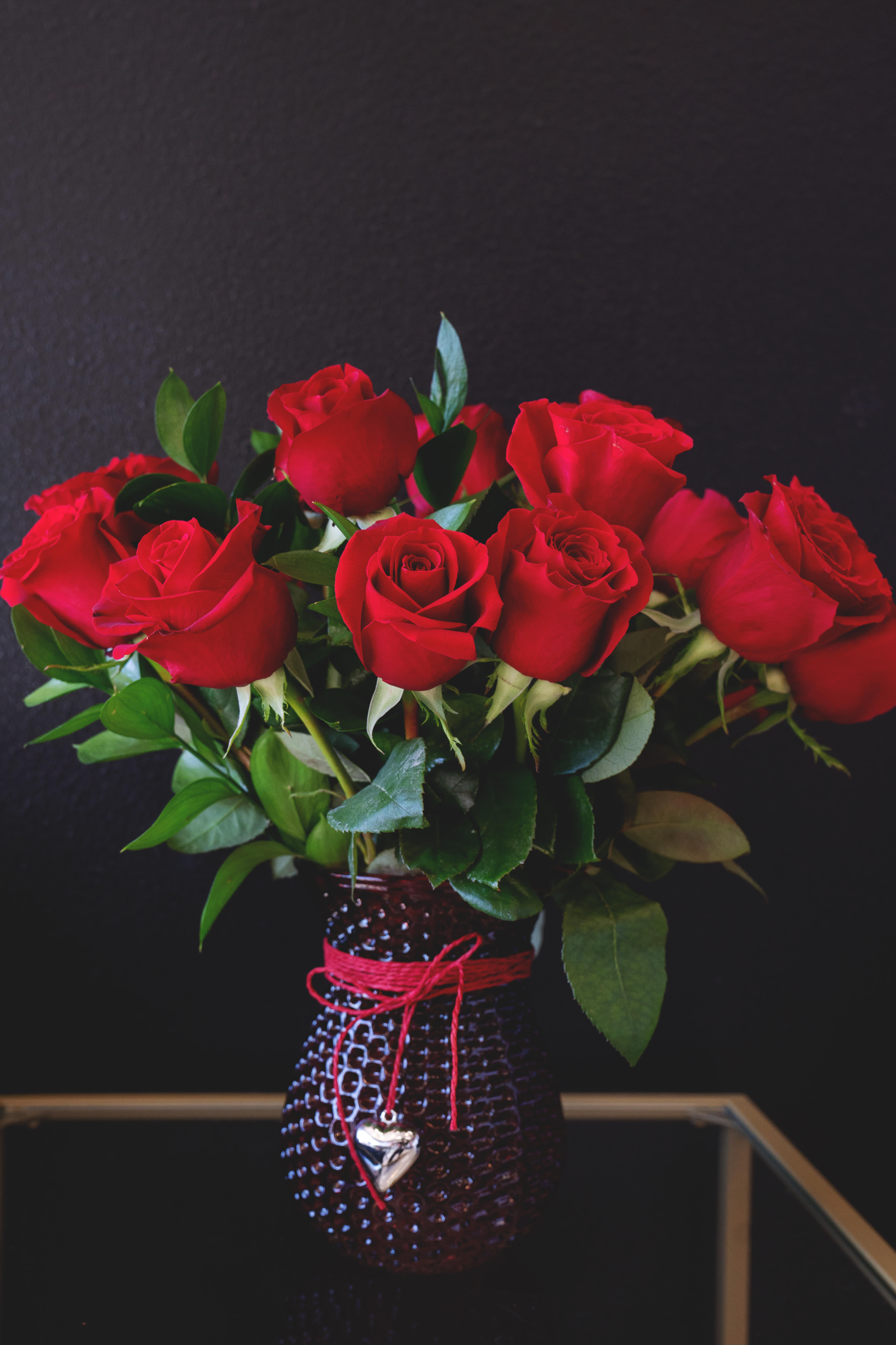 Red roses arranged in a textured vase with a red cord and heart charm