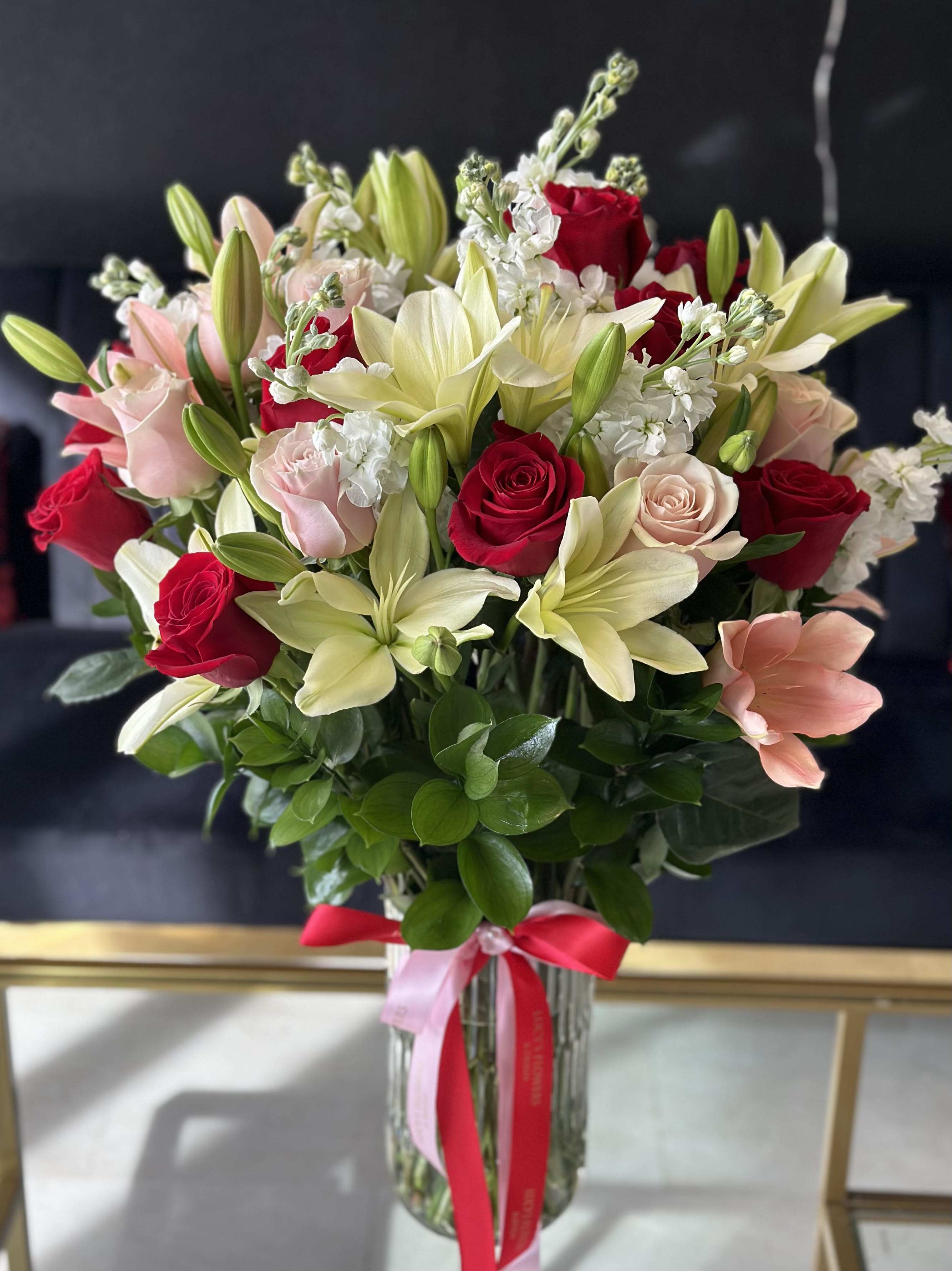 Bouquet of red and blush roses with pale lilies in a glass vase