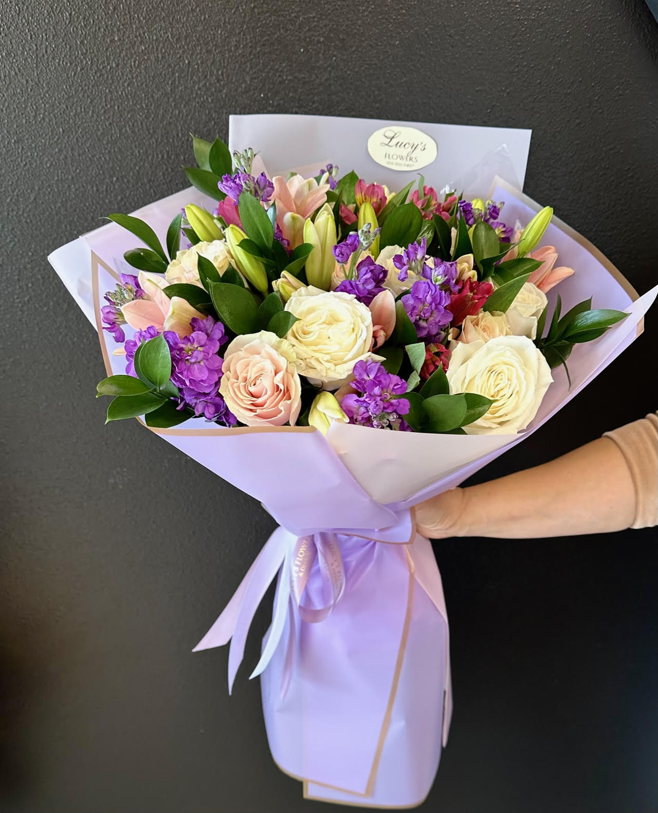 Bouquet of cream, blush, and purple flowers wrapped in lavender paper