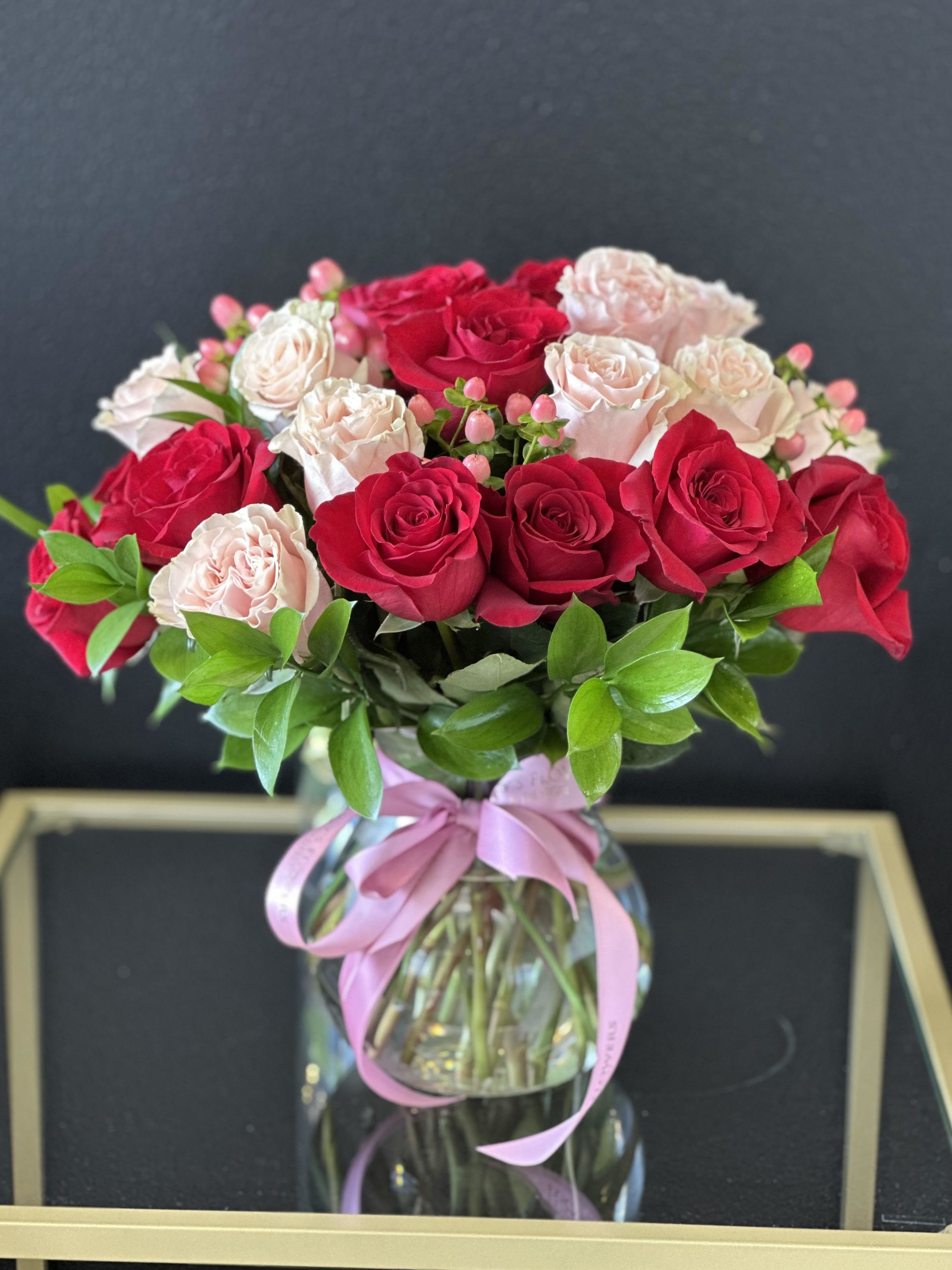 Bouquet of red and pale pink roses in a glass vase with a pink ribbon