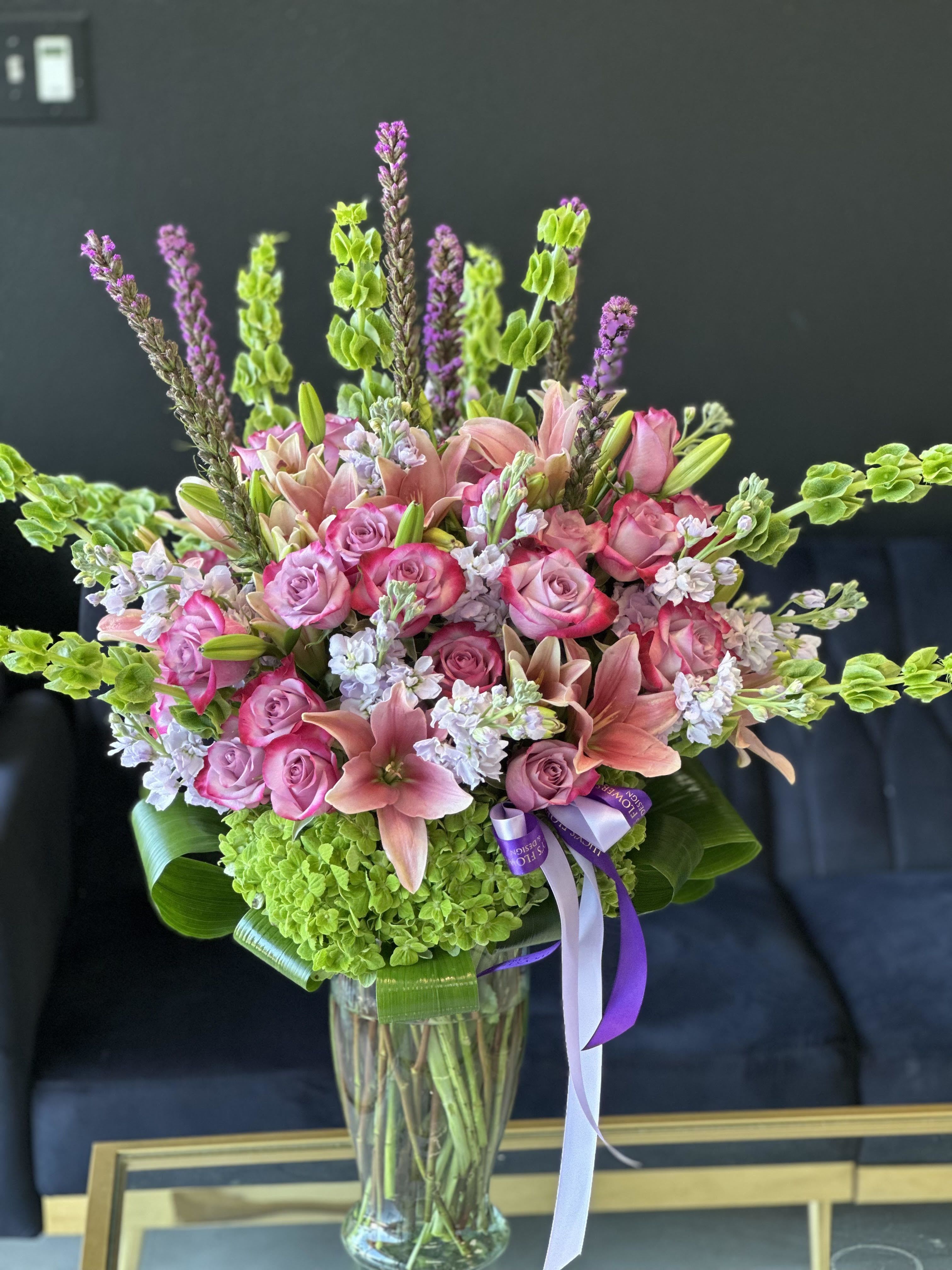 Pink roses and lilies arranged in a clear glass vase with green hydrangea and purple accents