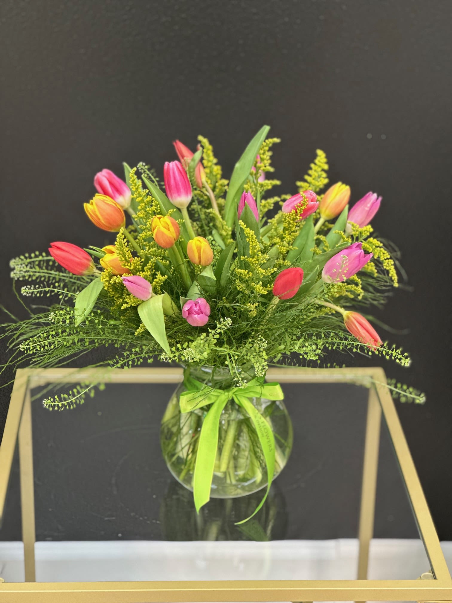 Colorful tulip bouquet in a round glass vase with a green ribbon