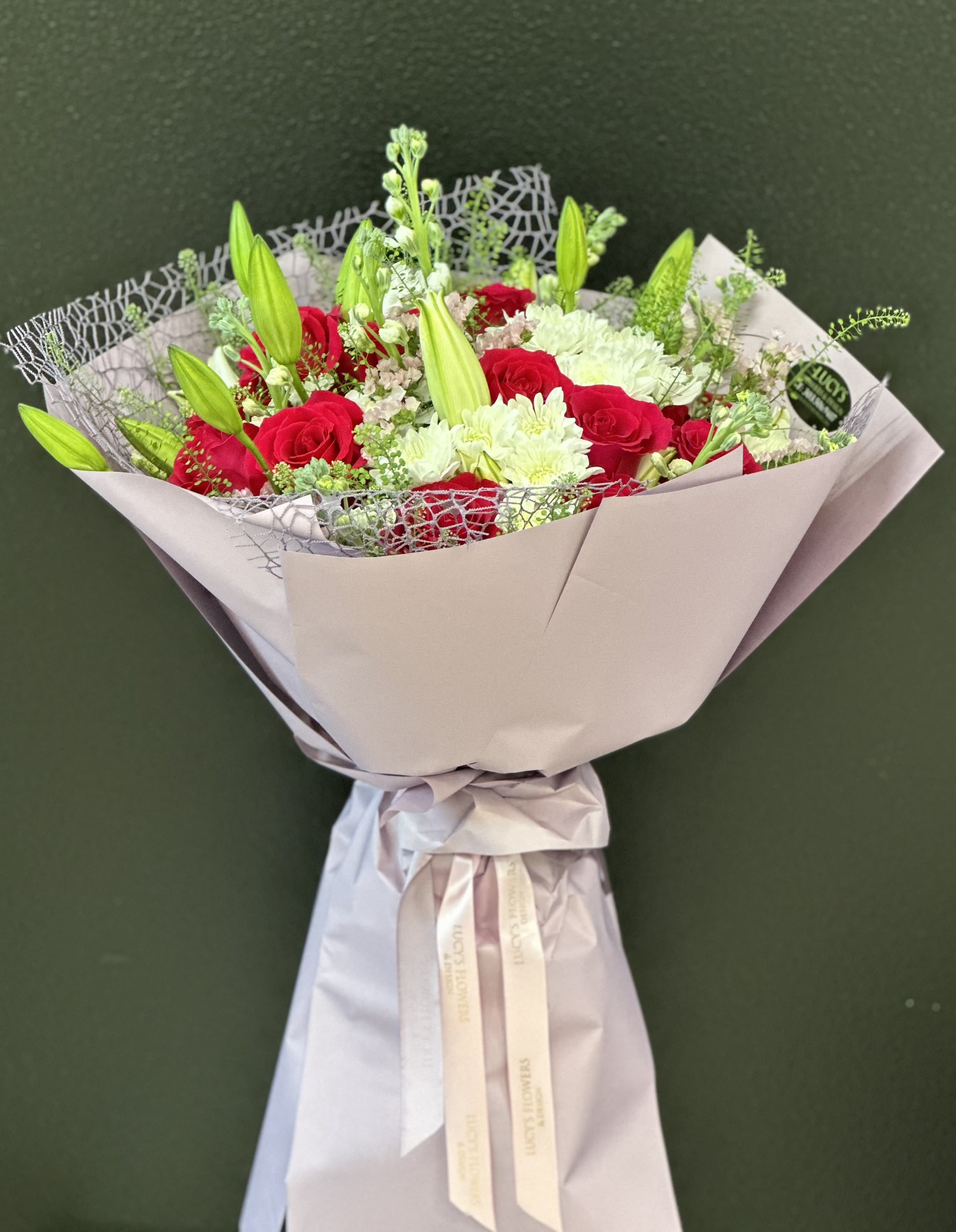 Bouquet of red roses and white lilies wrapped in pale paper