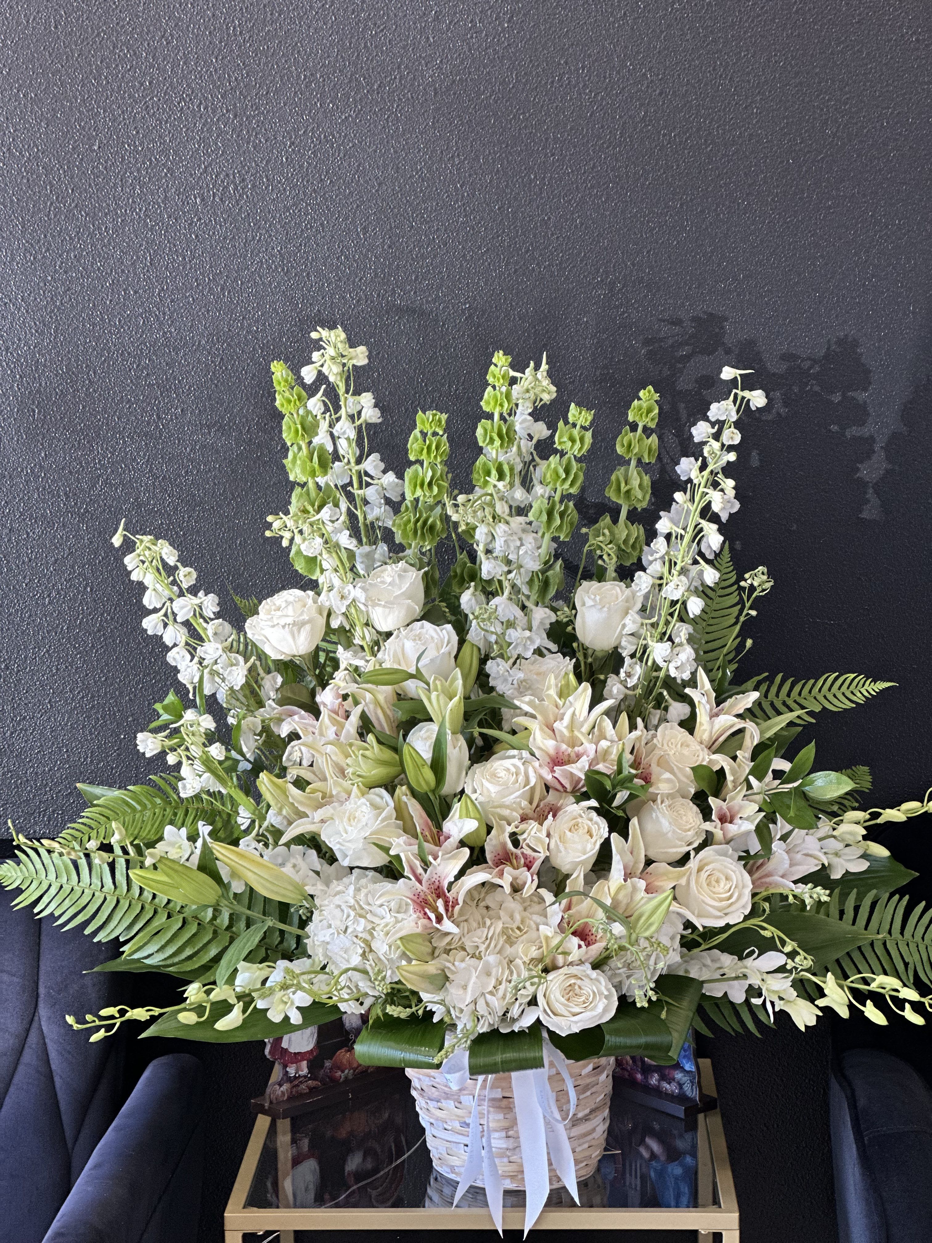 Hope - An all-white funeral basket featuring  lilies, roses, hydrangeas, and more framed by a backdrop of large leaves. Suitable for any type of funeral ceremony 