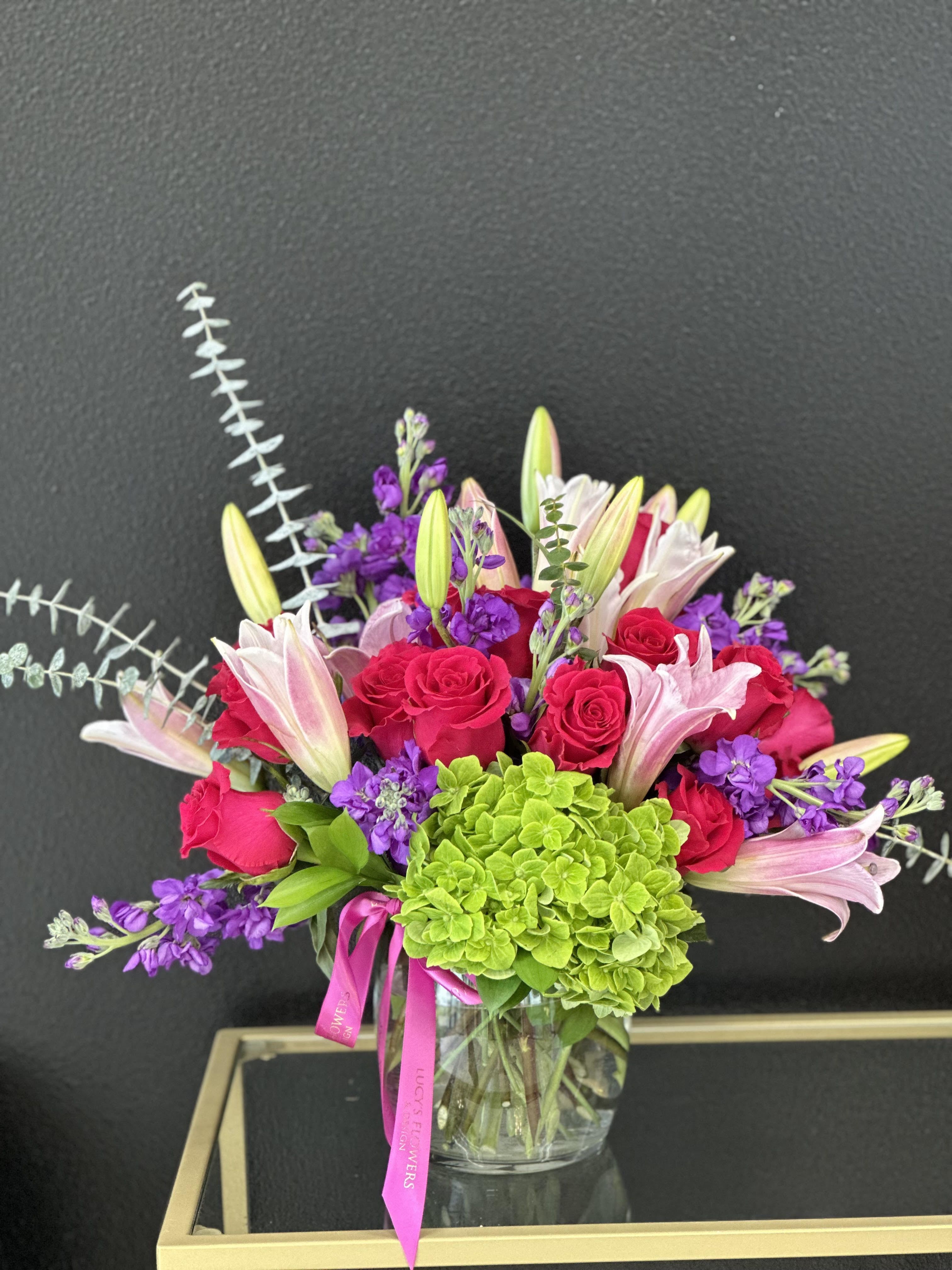 Bouquet of pink roses, lilies, and purple flowers in a glass vase