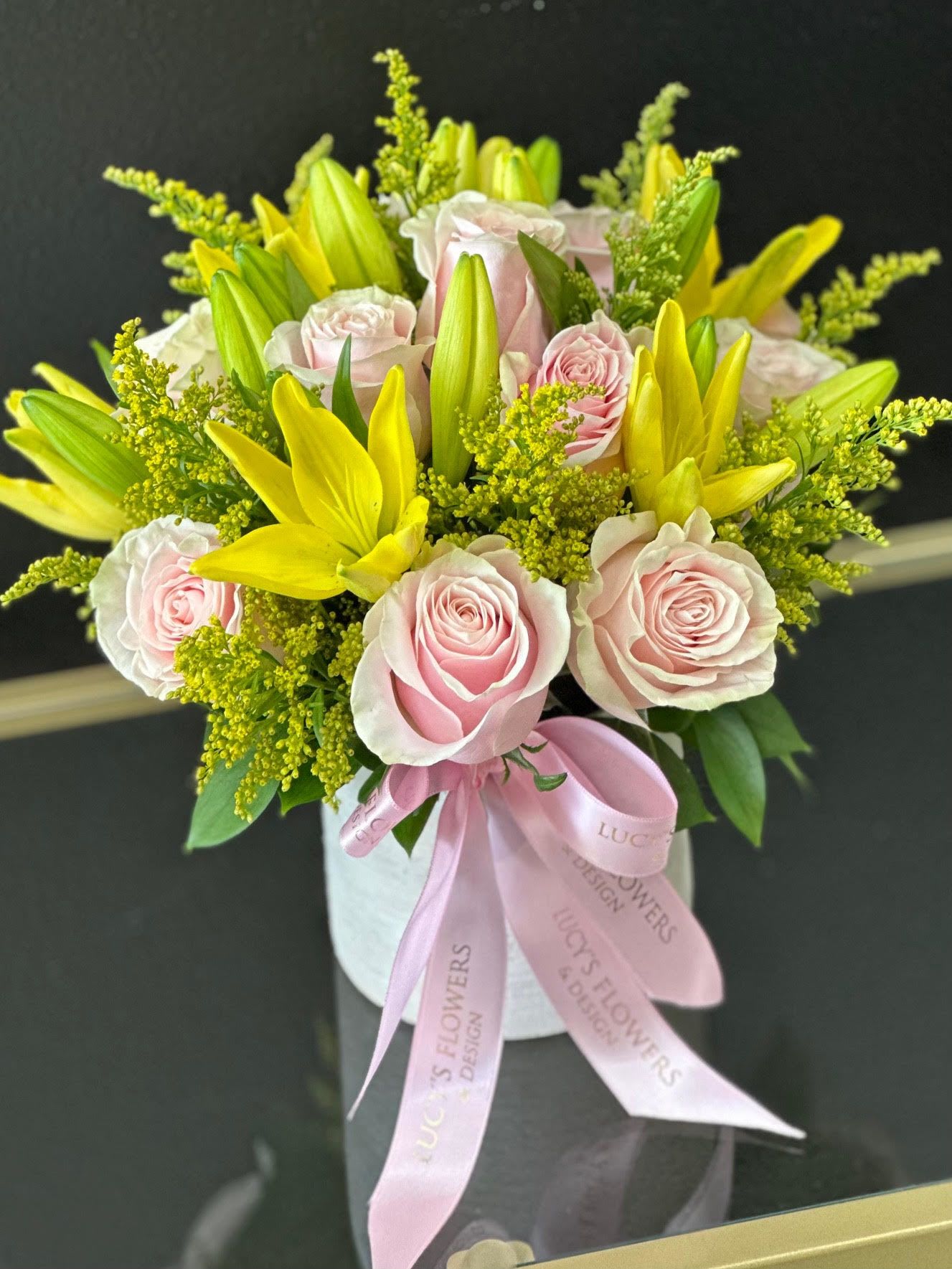 Pink roses and yellow lilies arranged in a white box with a pink ribbon