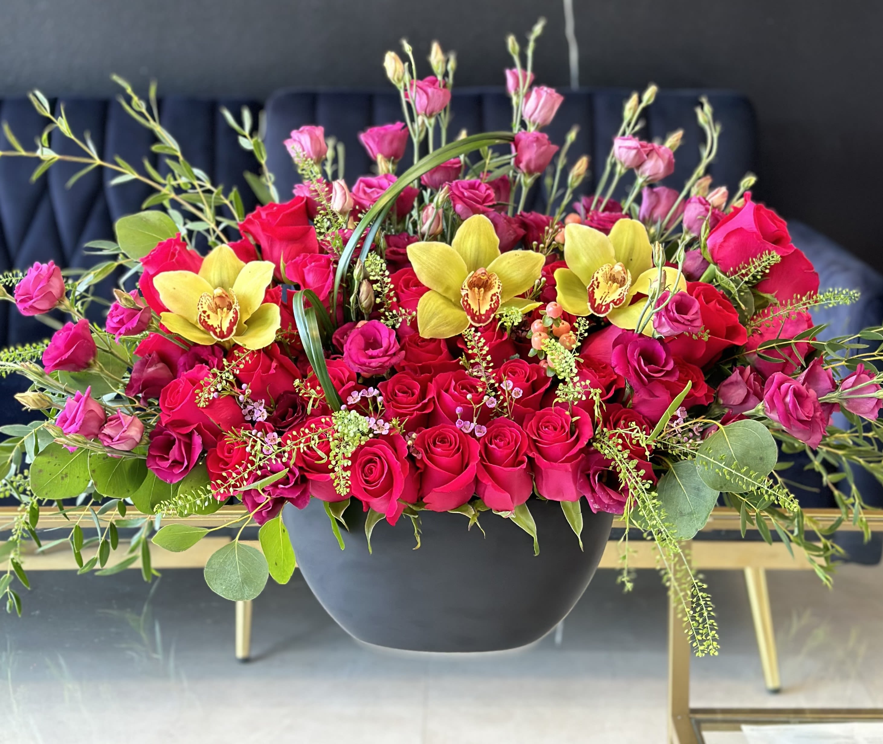 Pink and red roses with yellow orchids in a black bowl vase