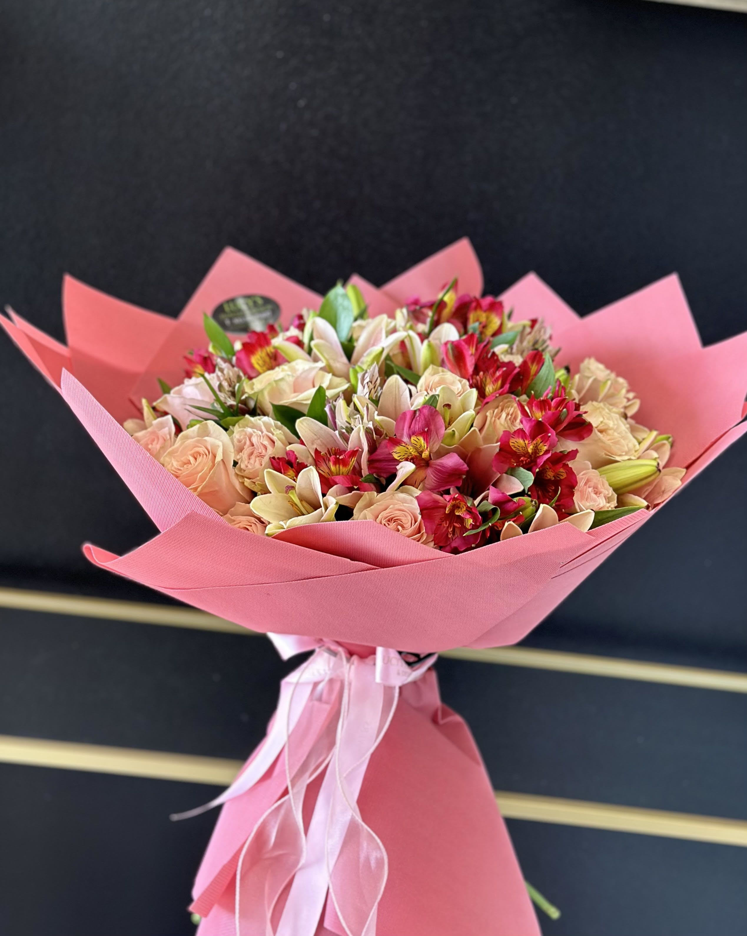 Pink-wrapped bouquet of peach roses and mixed lilies