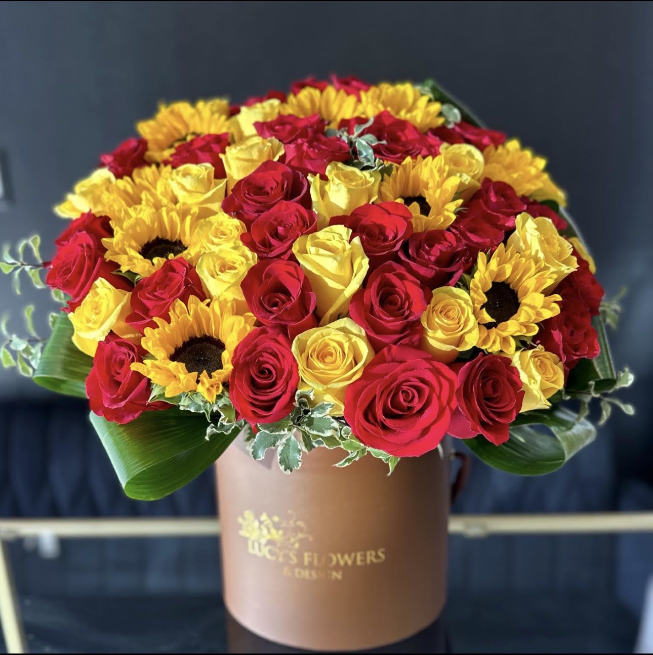 "Autumn Glimmer" - Autumn glimmer is a quintessential fall arrangement featuring our signature  box and a variety of fun fall flowers and accents. This arrangement is pure fun and elegance that the recipient will for enjoy. Send this to impress! Perfect for the autumn equinox, Halloween or Thanksgiving.  Arrangement Includes: -Lucy's Signature Medium Size Box -Fresh Cut Roses, Sunflowers, Lilies -Custom Greeting Card -Care Instructions