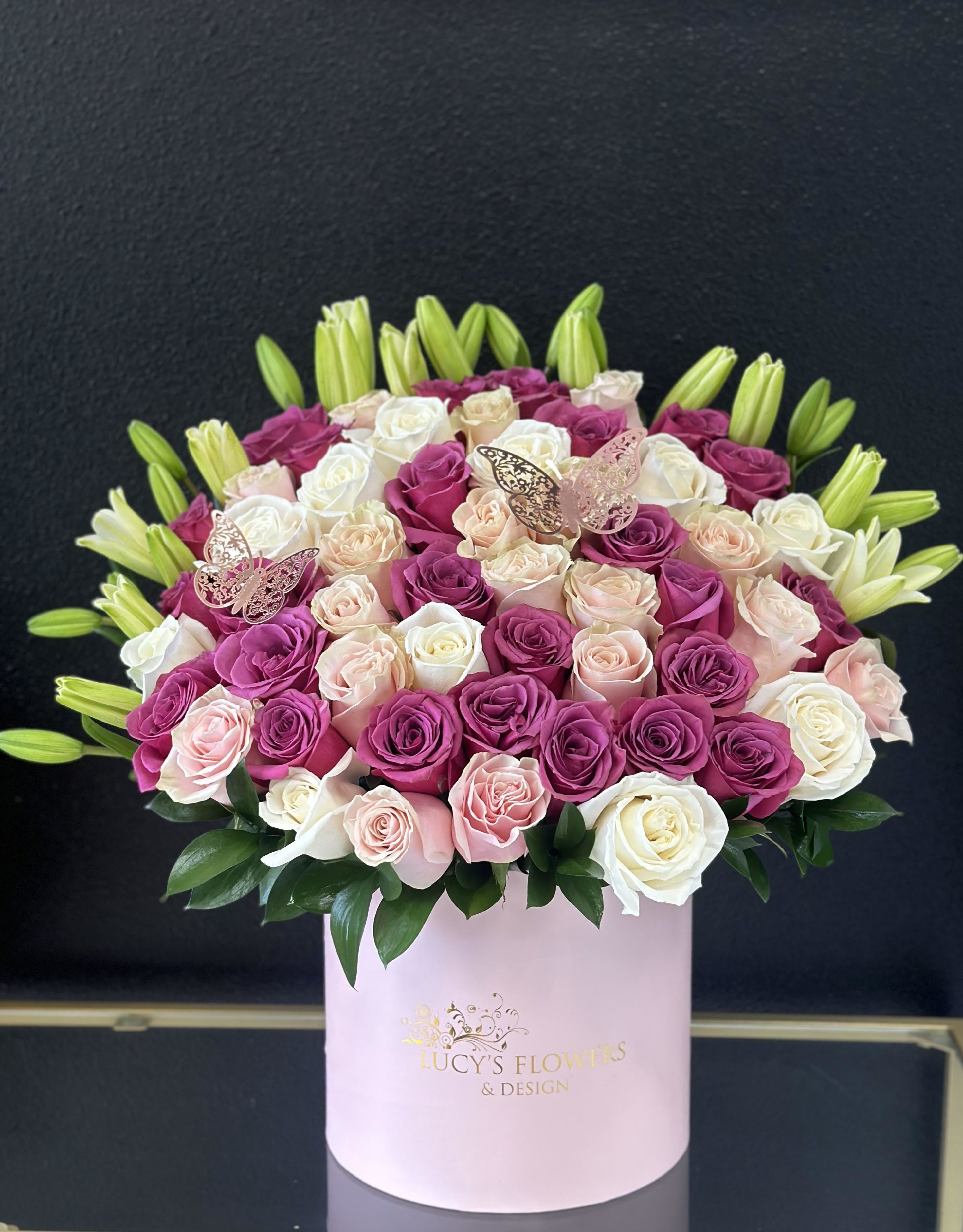 Pink, white, and peach roses in a round pink box with lily buds