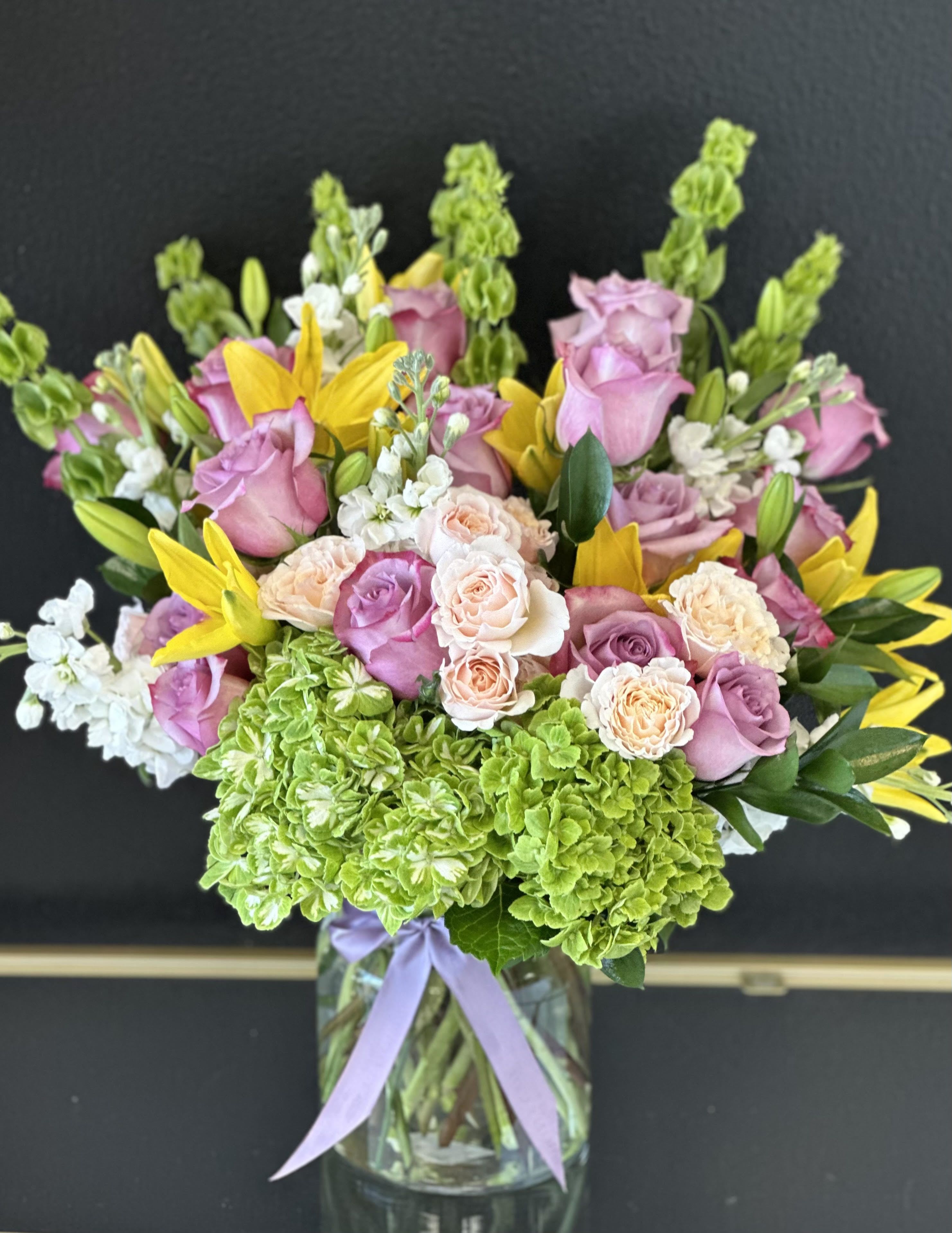 Bouquet of pink roses, green hydrangeas, and yellow lilies in a glass vase