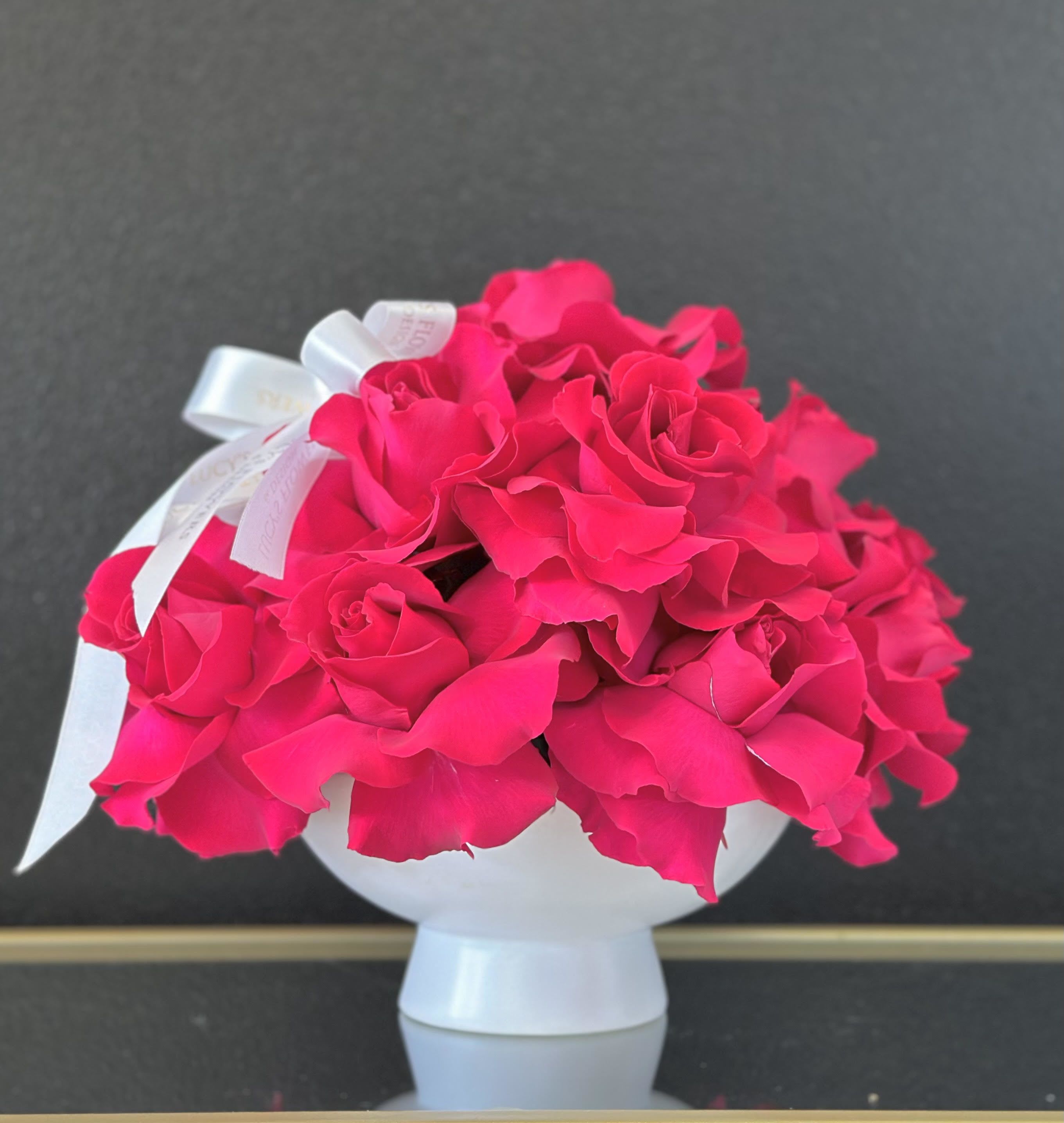 Bright pink rose bouquet in a white vase with a ribbon bow