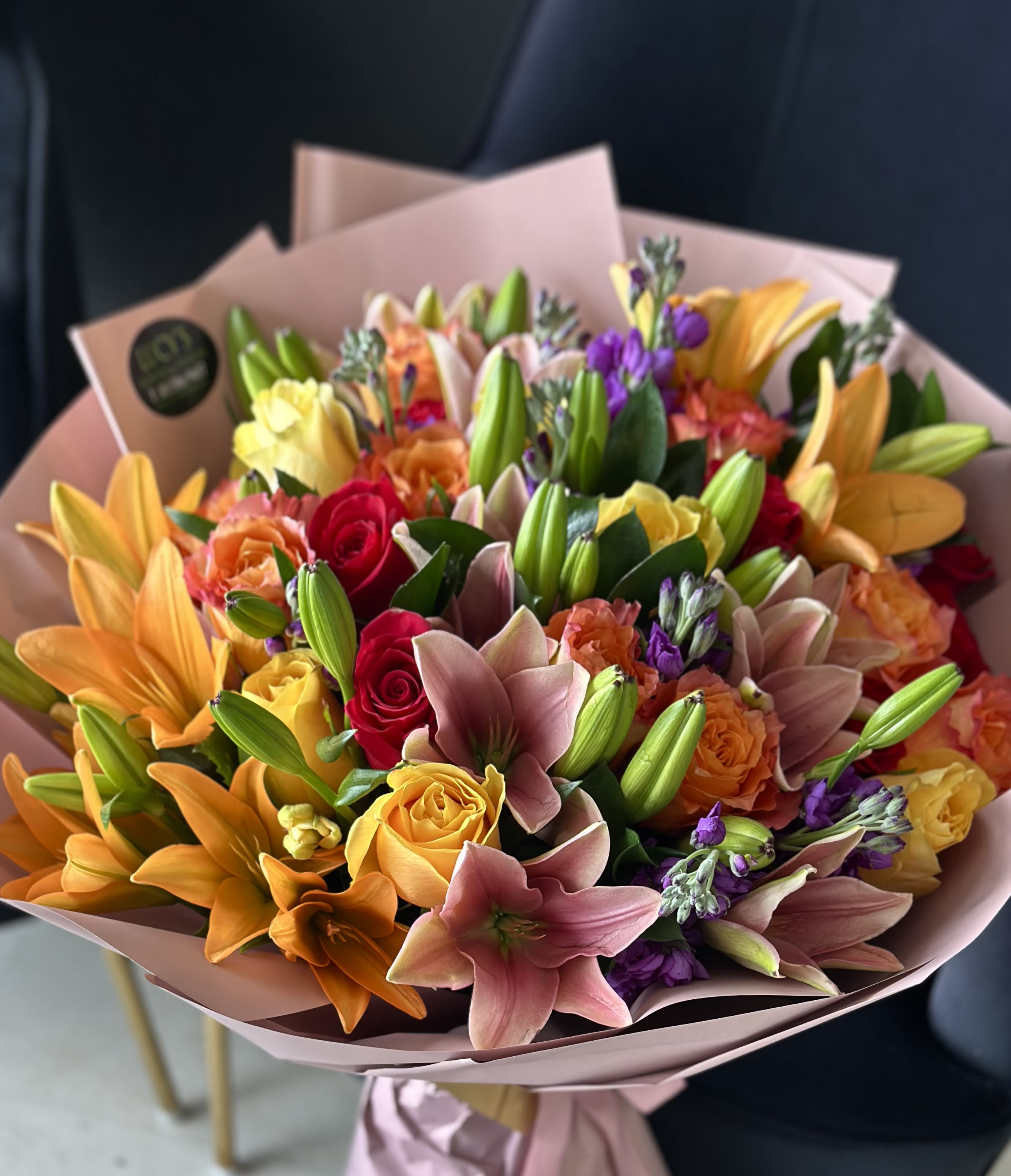 Mixed bouquet of lilies, roses, and purple flowers wrapped in pink paper