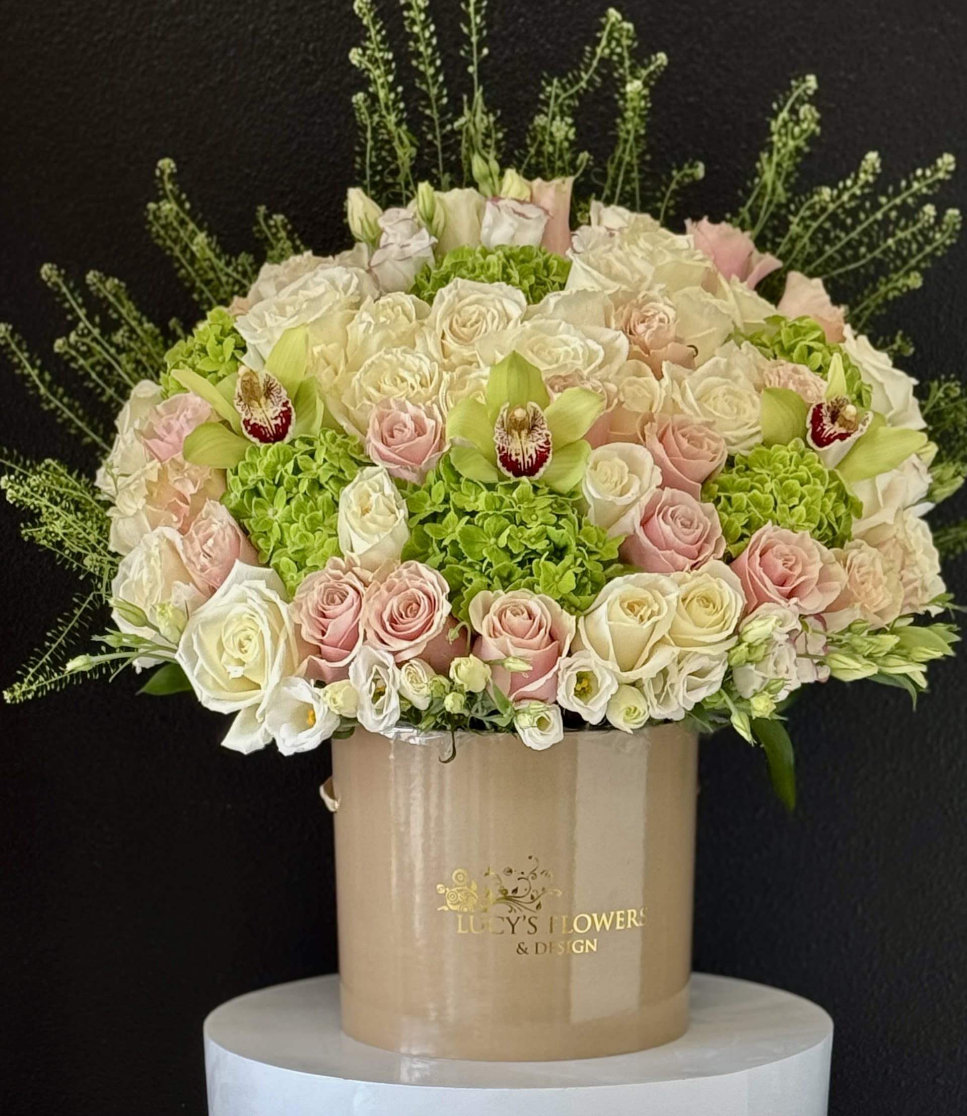 Round bouquet of pale roses and green orchids in a beige hatbox
