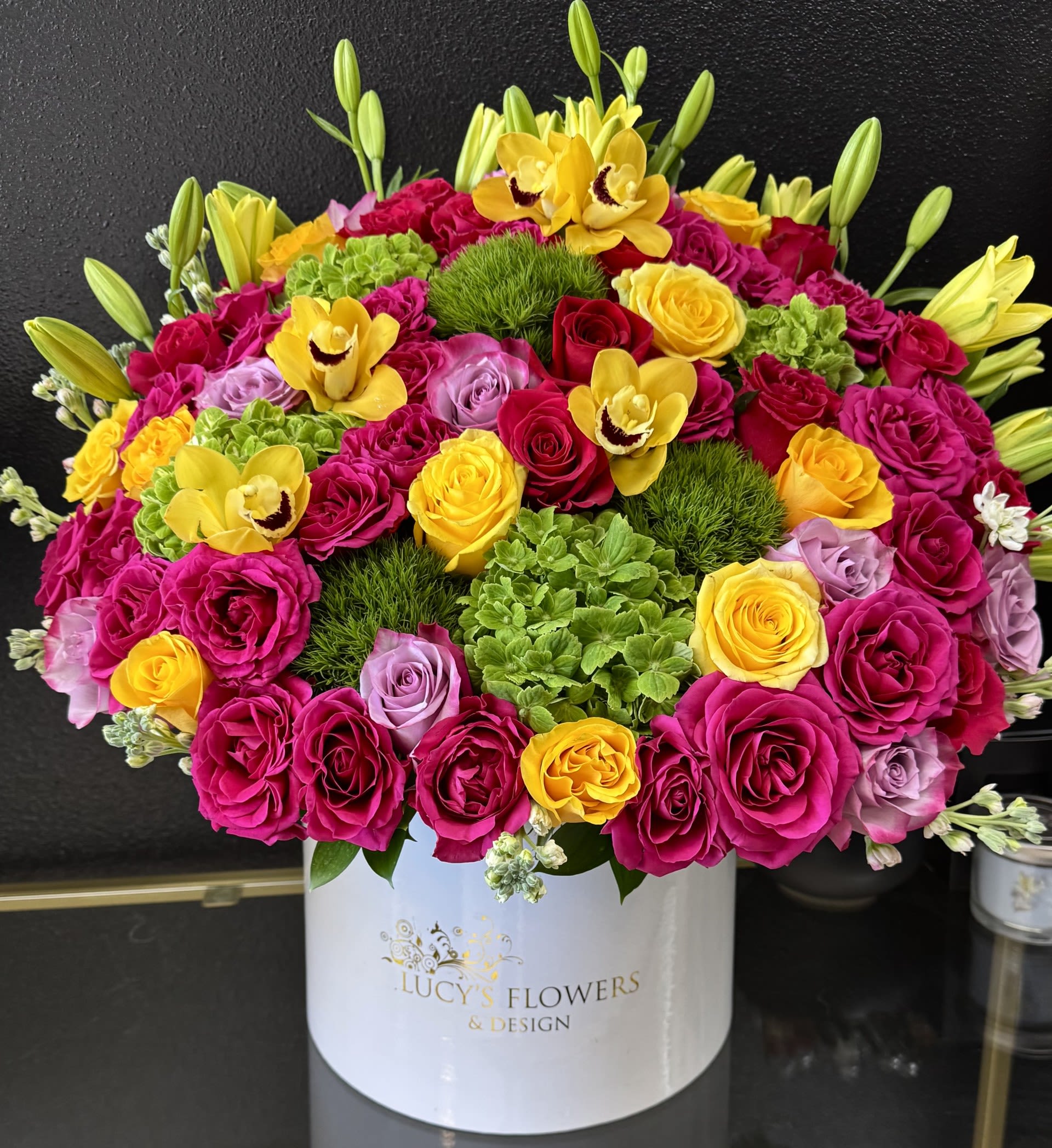 Enchanted Love  - This beautiful lavender arrangement is guaranteed to brighten someone's day. Enchanted Love  is perfect for someone's birthday or for anyone that needs cheering up.  Arrangement Includes: -Fresh cut lavender roses, orchids and other flowers -Lucy's Flowers &amp; Design Medium box (9.75" Dia. x 9.25" H) -Custom Greeting Card -Care Instructions   