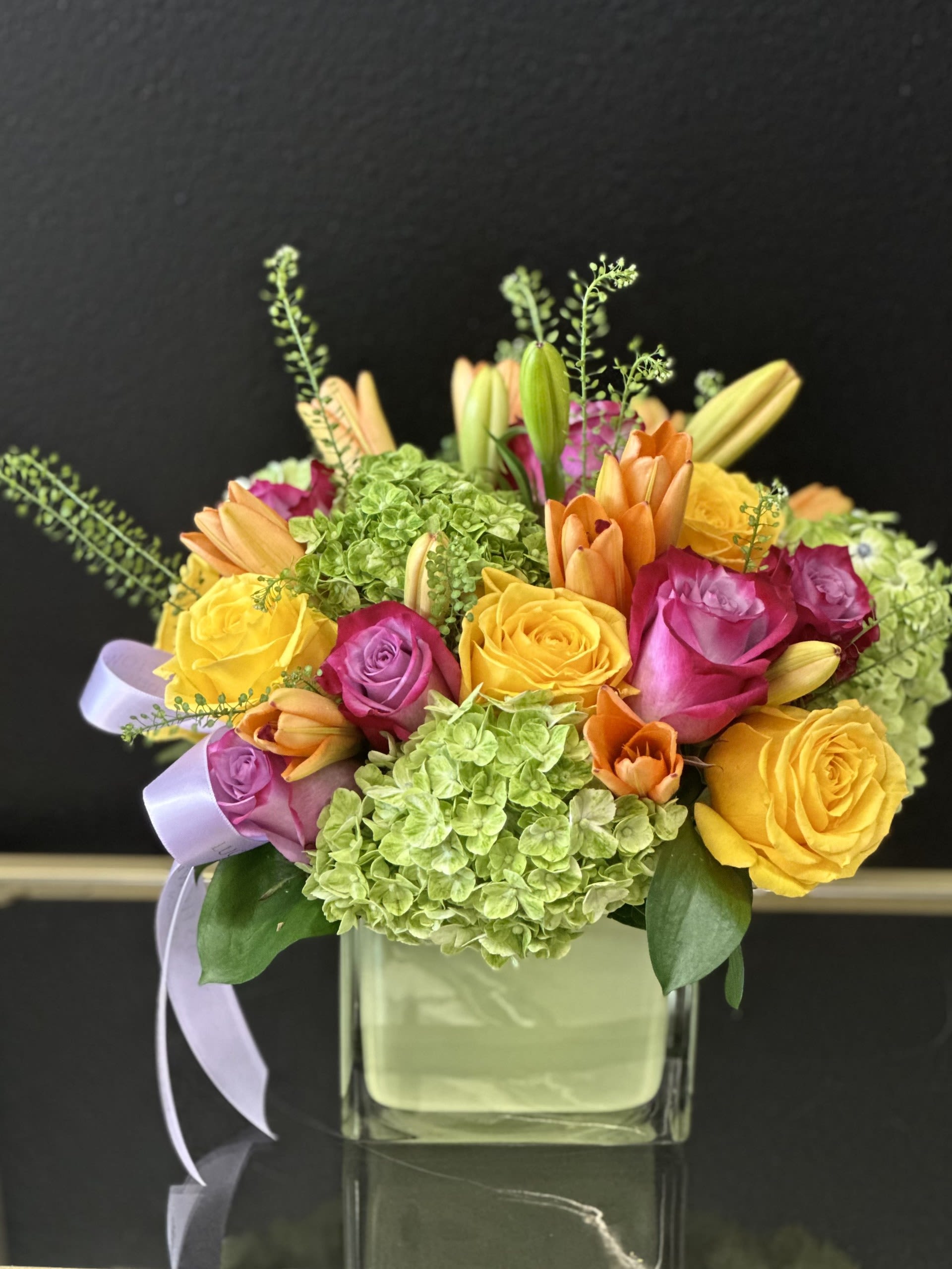 Colorful bouquet of roses, hydrangeas, and lilies in a square glass vase