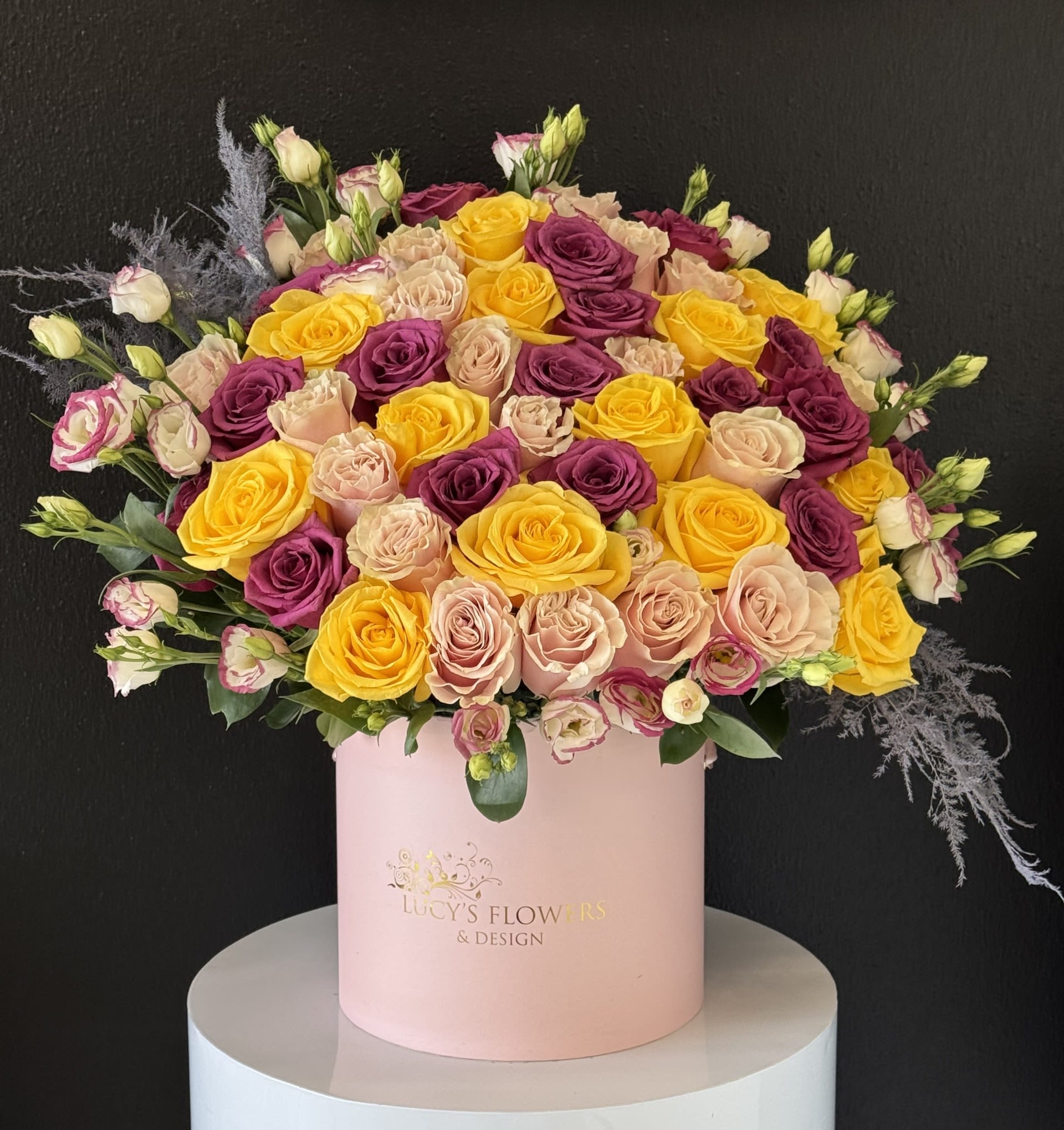 Large bouquet of yellow, blush, and purple roses in a pink hat box