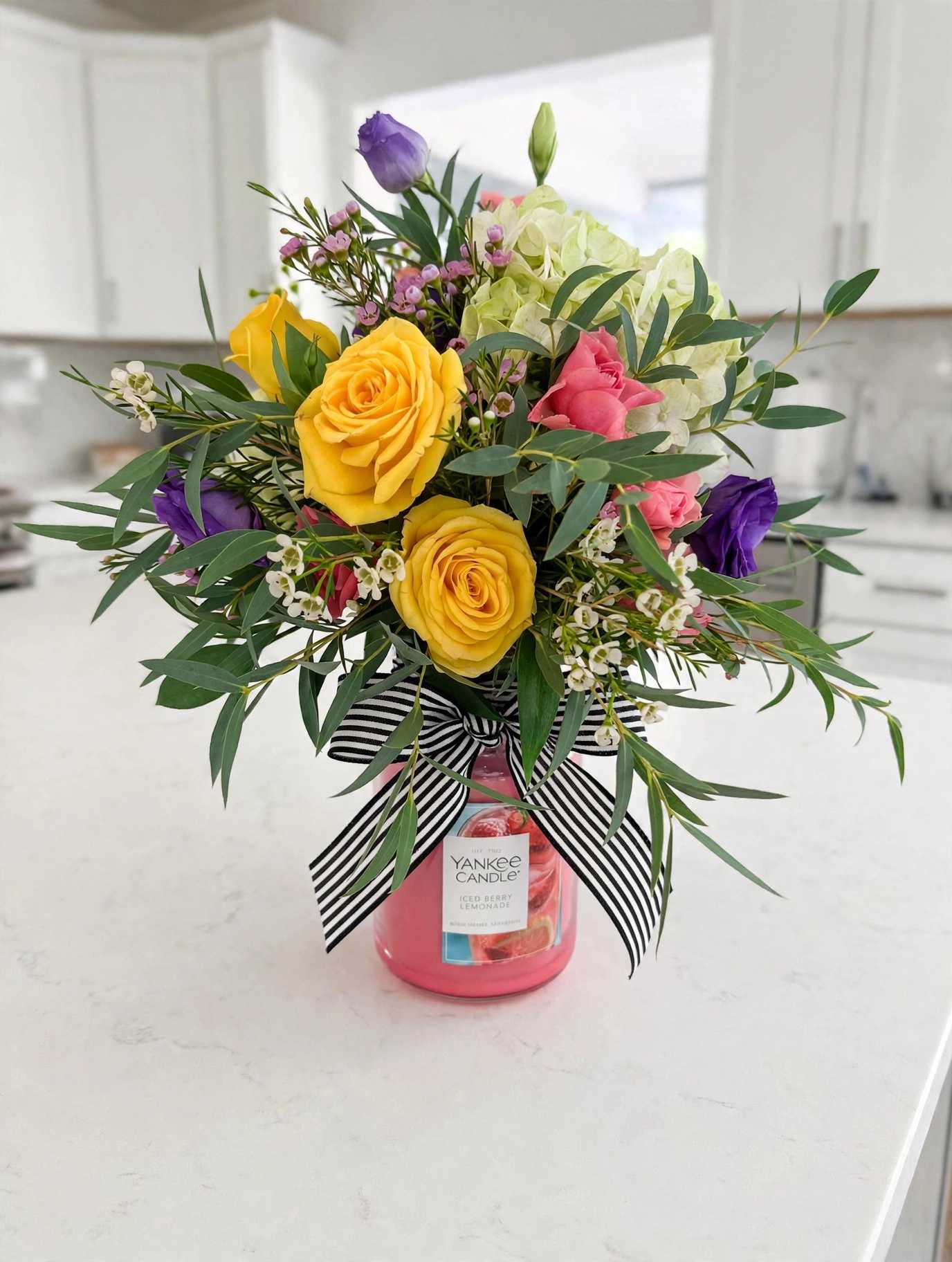 Bouquet of yellow, pink, purple, and white flowers in a pink candle jar