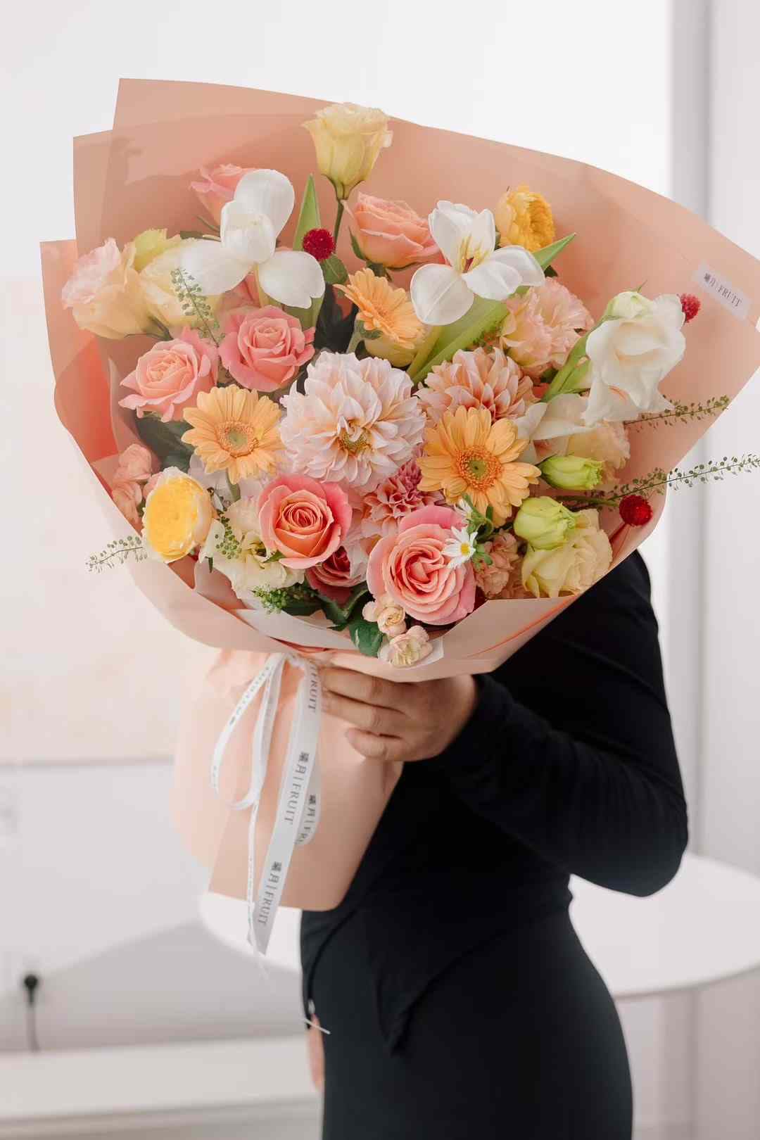 Large bouquet of pink, peach, and white flowers wrapped in peach paper
