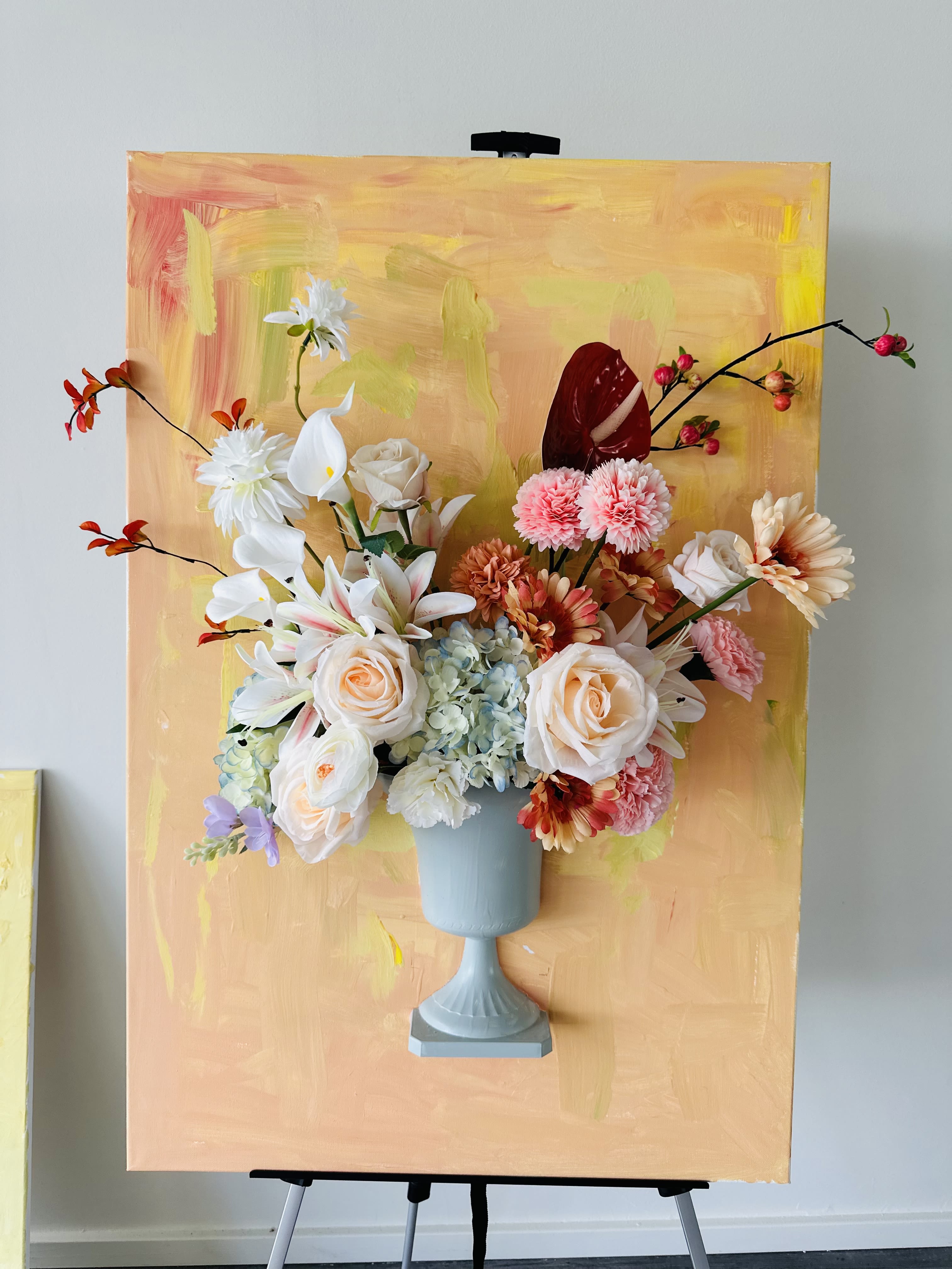 Mixed floral arrangement in a blue pedestal vase against a painted backdrop