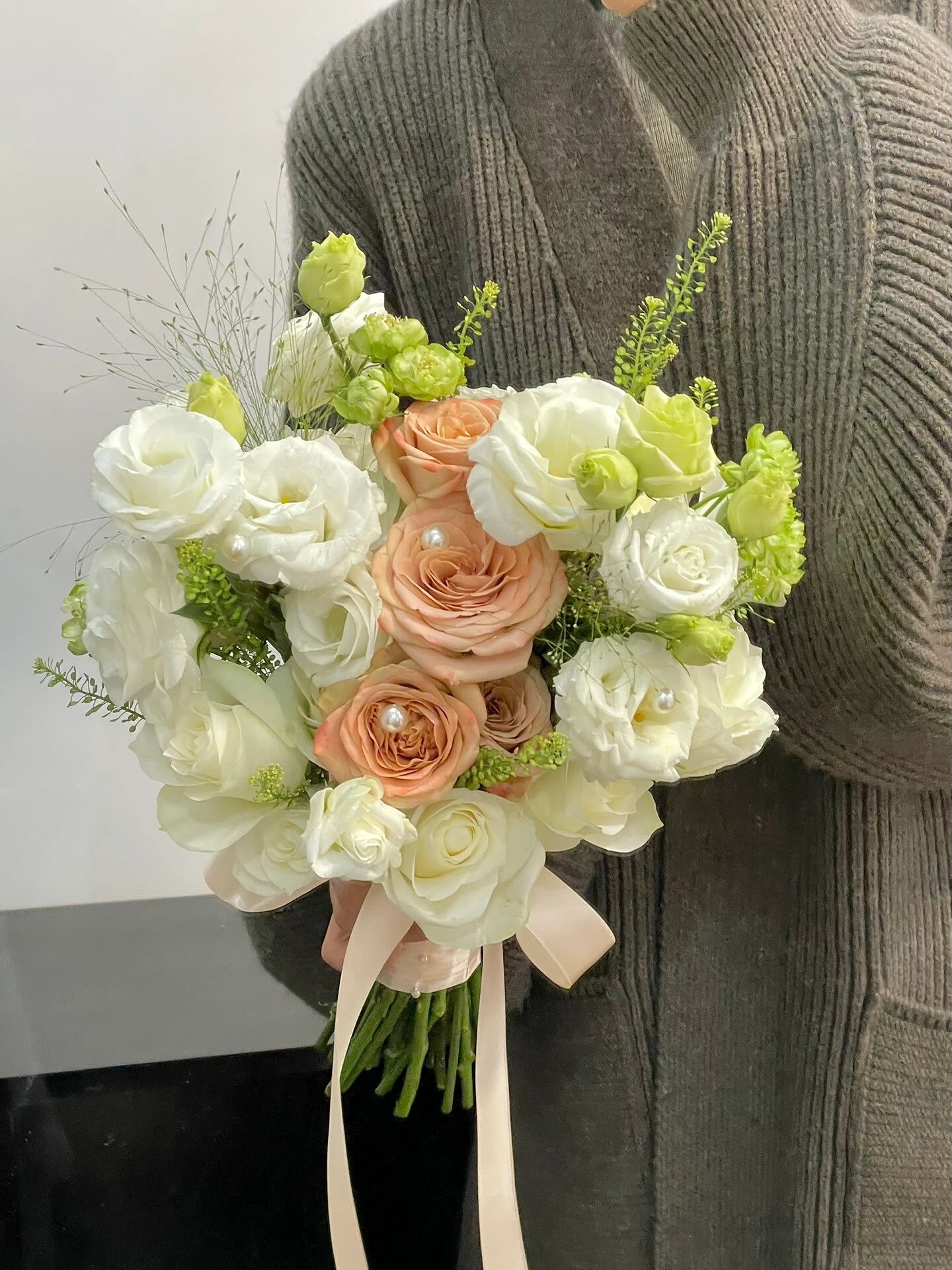 Bouquet of white and peach roses with pale green accents and ribbon