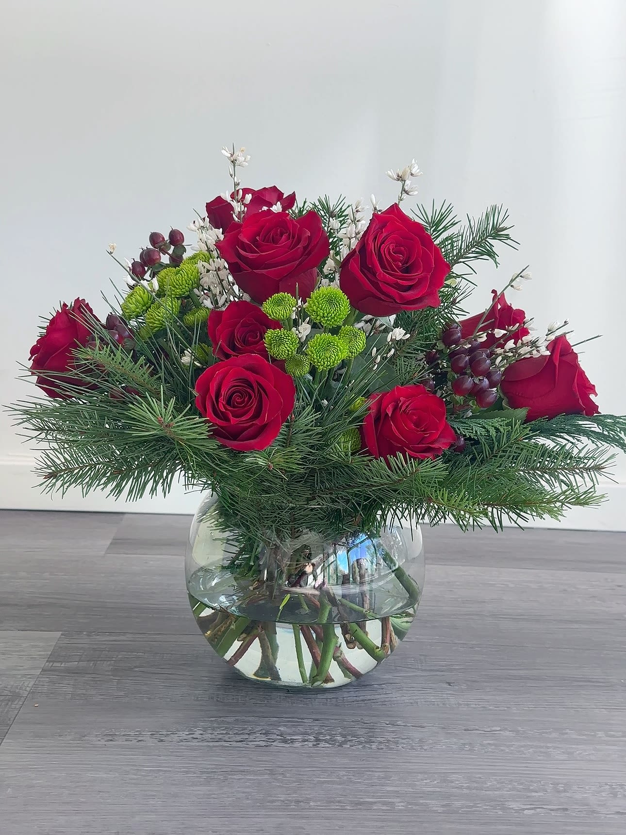 Red roses in a glass vase with pine and small white accents