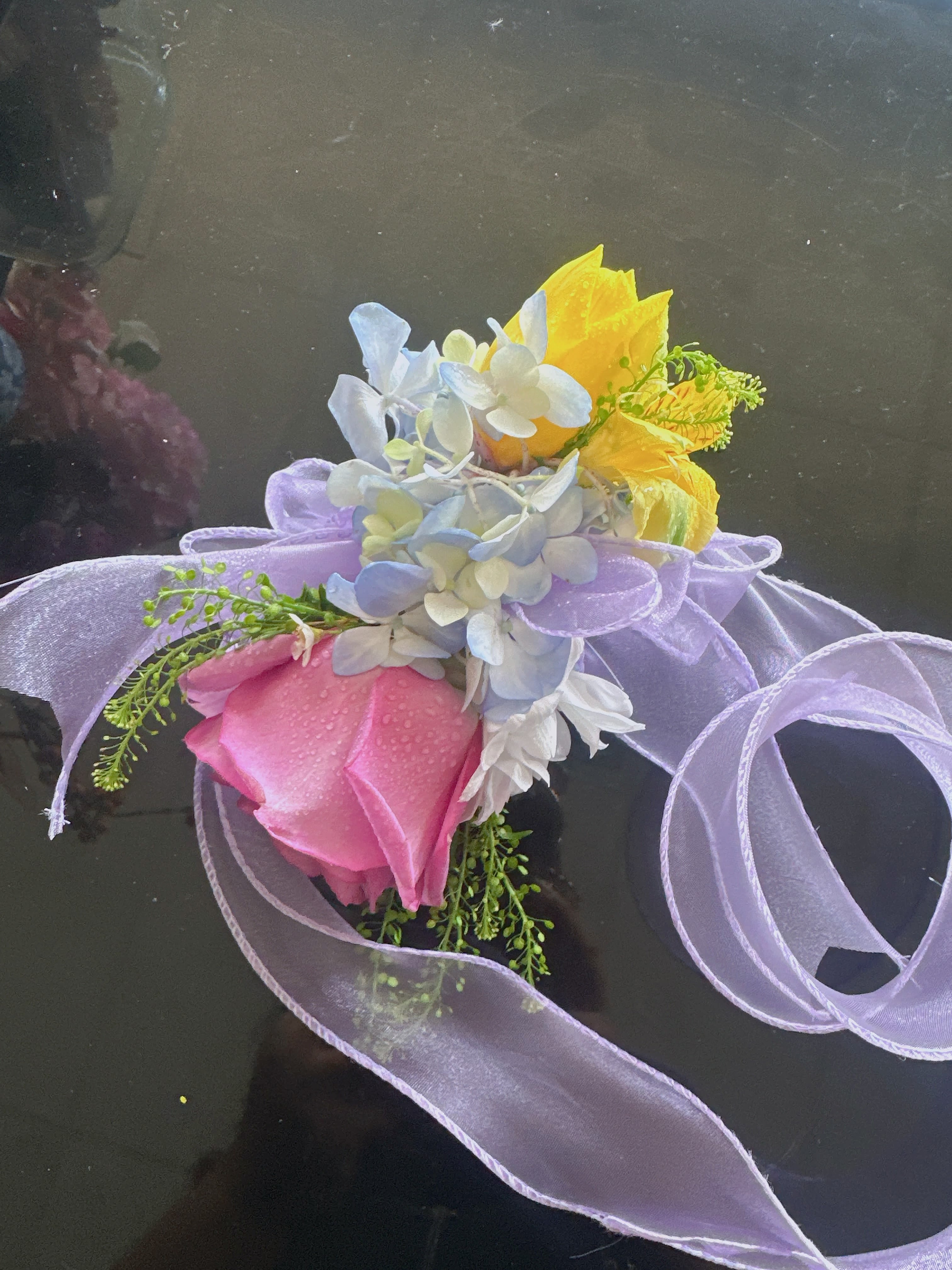 Small bouquet with pink and yellow roses and pale blue flowers tied with lavender ribbon