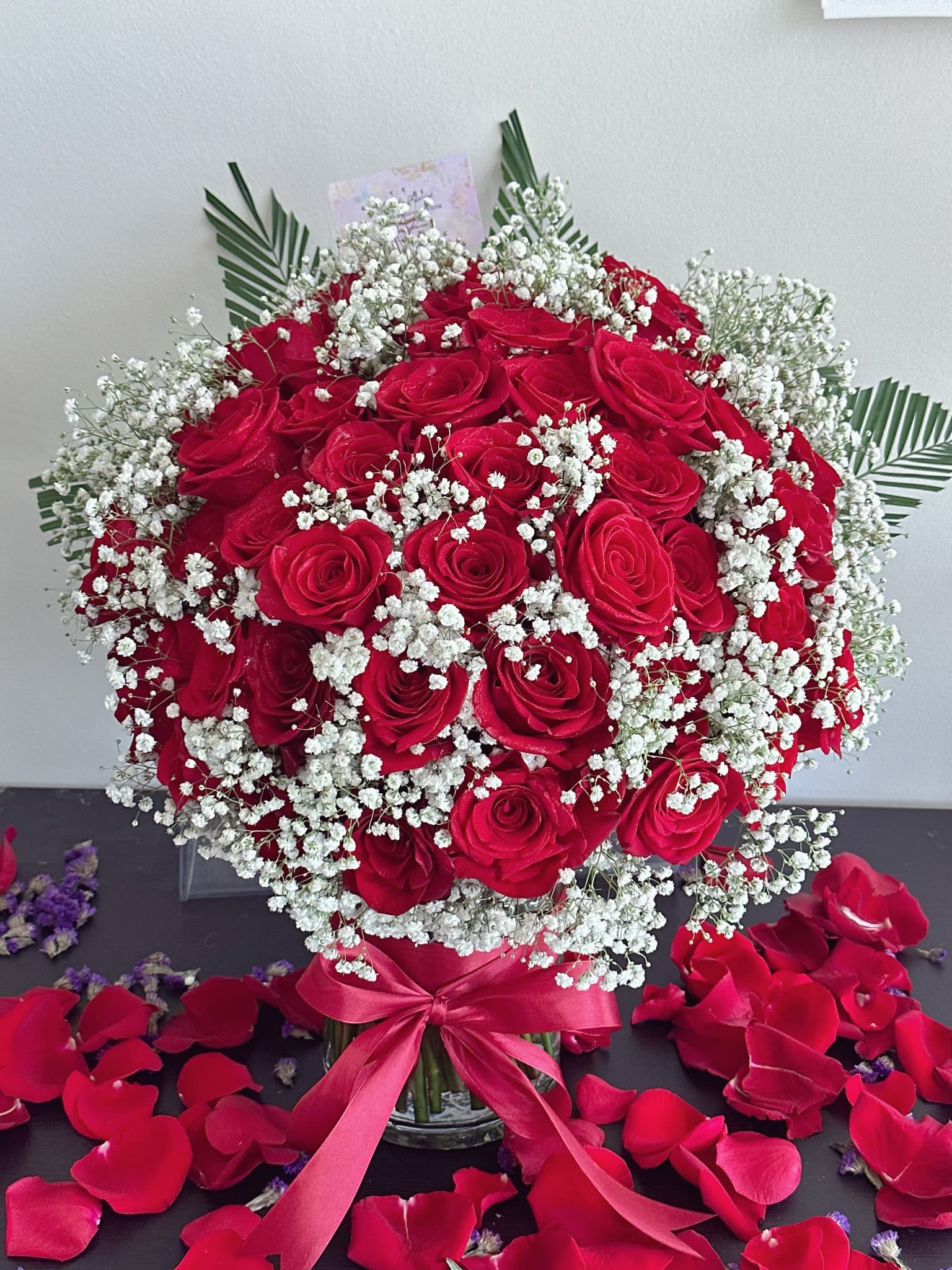 Red rose bouquet with baby's breath in a glass vase and ribbon