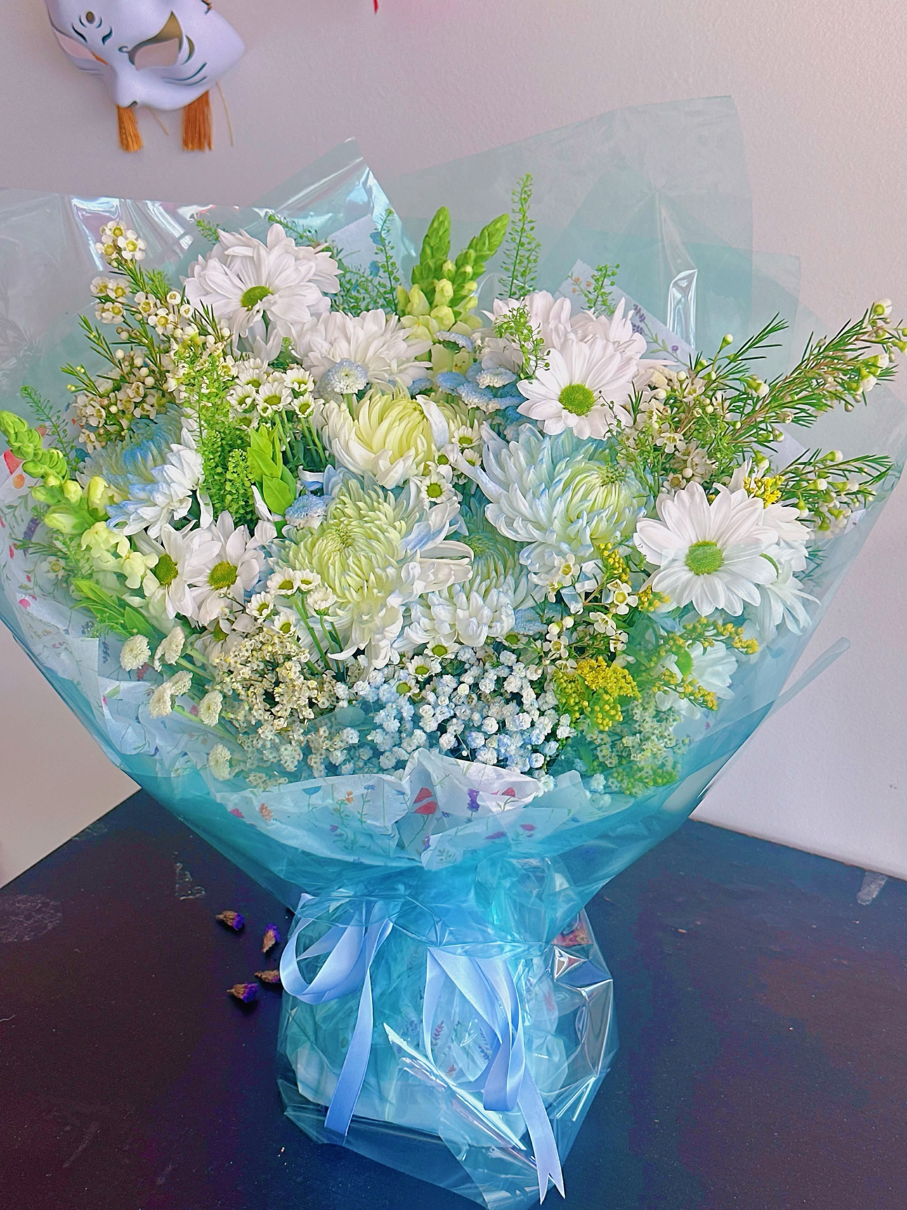 Bouquet of white daisies and pale blue flowers wrapped in blue cellophane