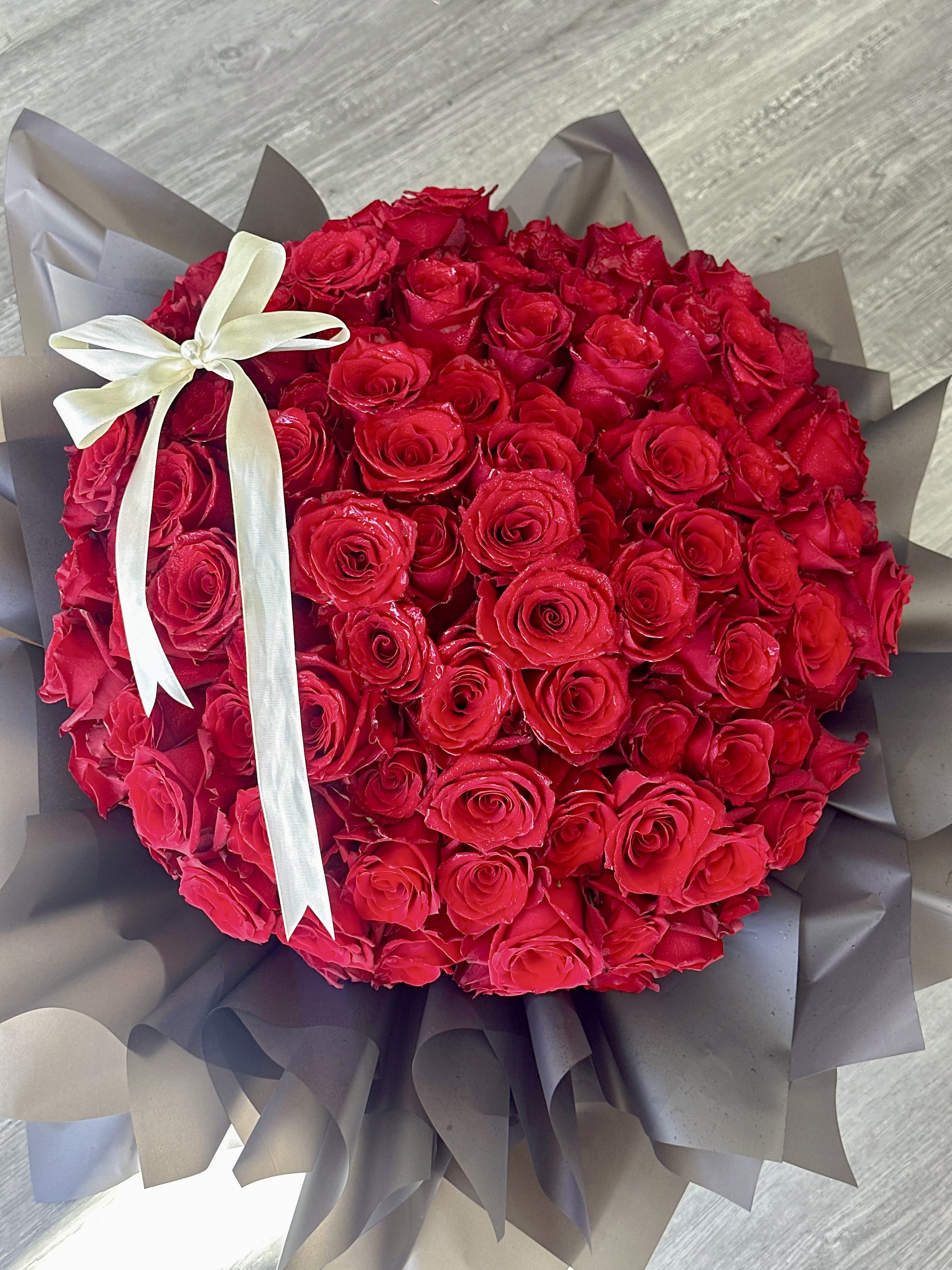 Round bouquet of red roses wrapped in dark paper with a white ribbon